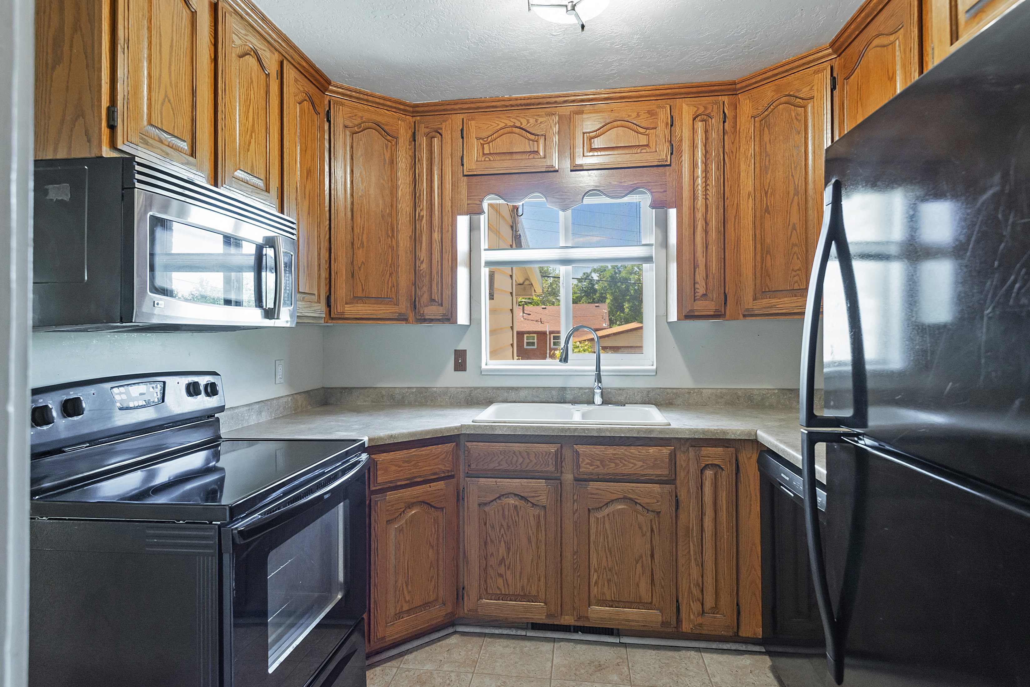 Kitchen featuring abundant wood cabinetry, laminate countertops, a stainless steel microwave, and a double basin sink with a window above