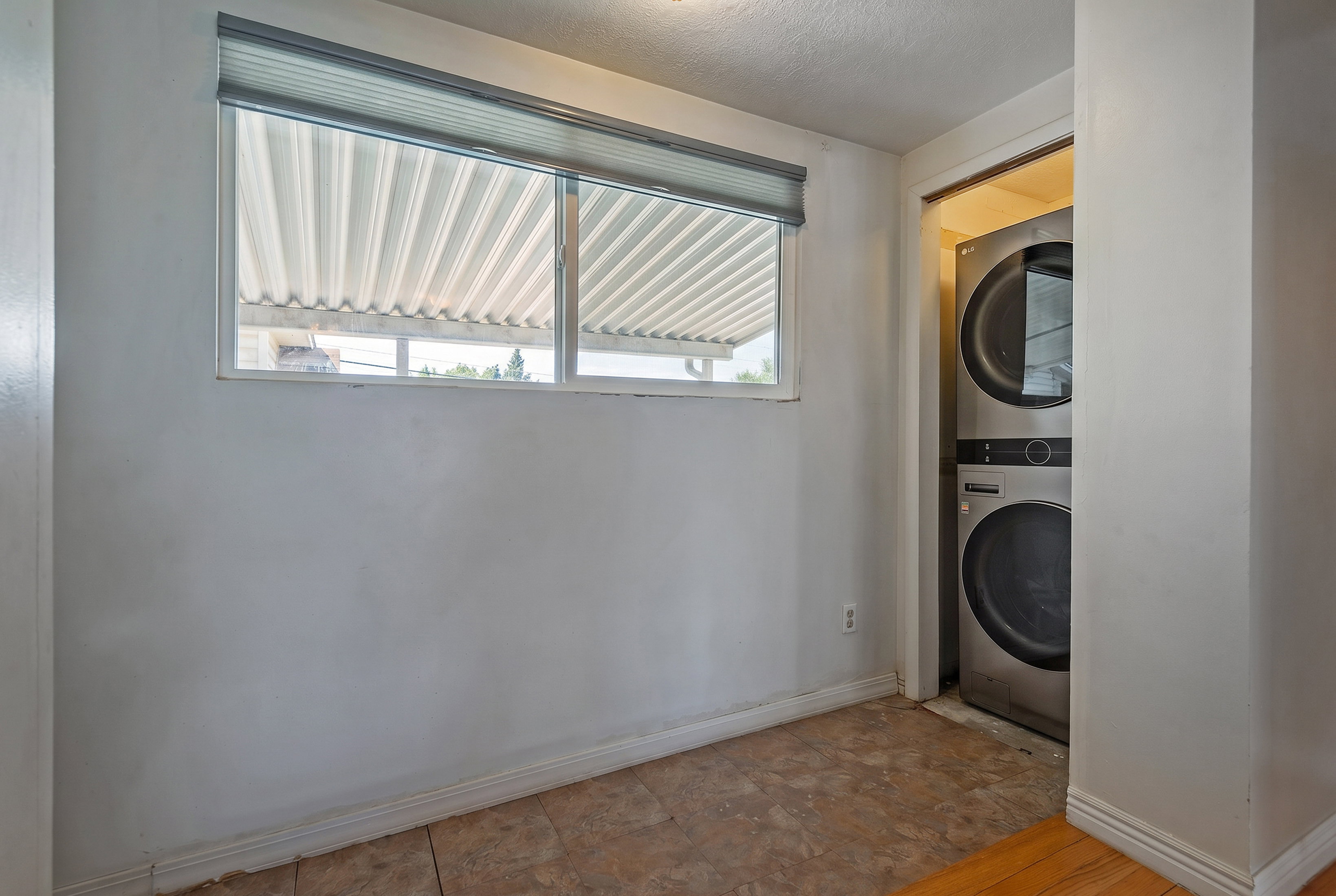 Dedicated laundry space featuring a stacked washer and dryer unit, complemented by a window with blinds and tile flooring