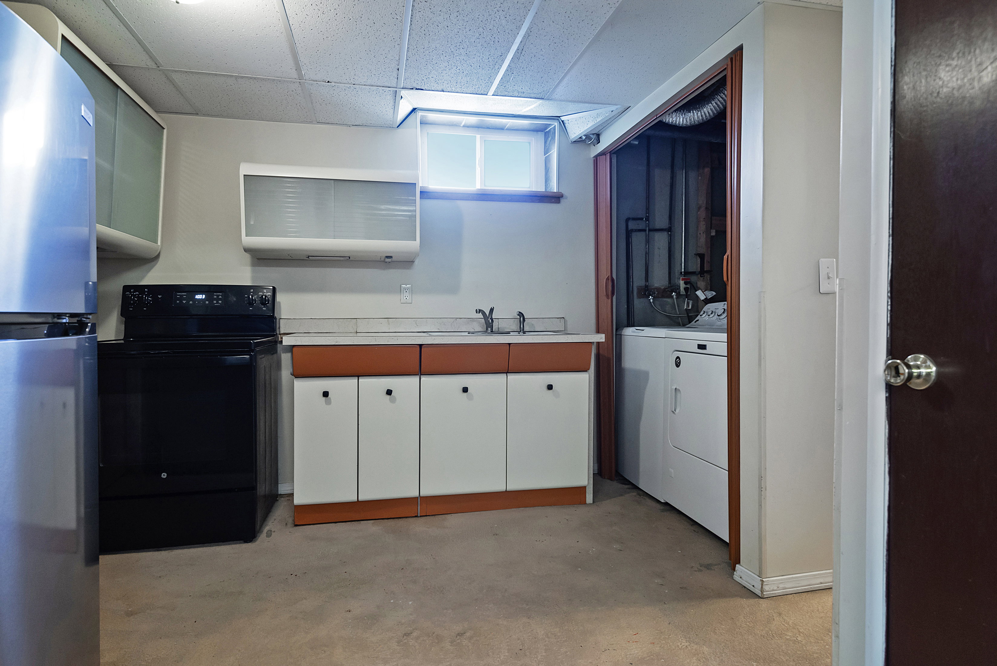 Utility area featuring a stainless steel refrigerator, black electric range, and a sink with lower cabinetry