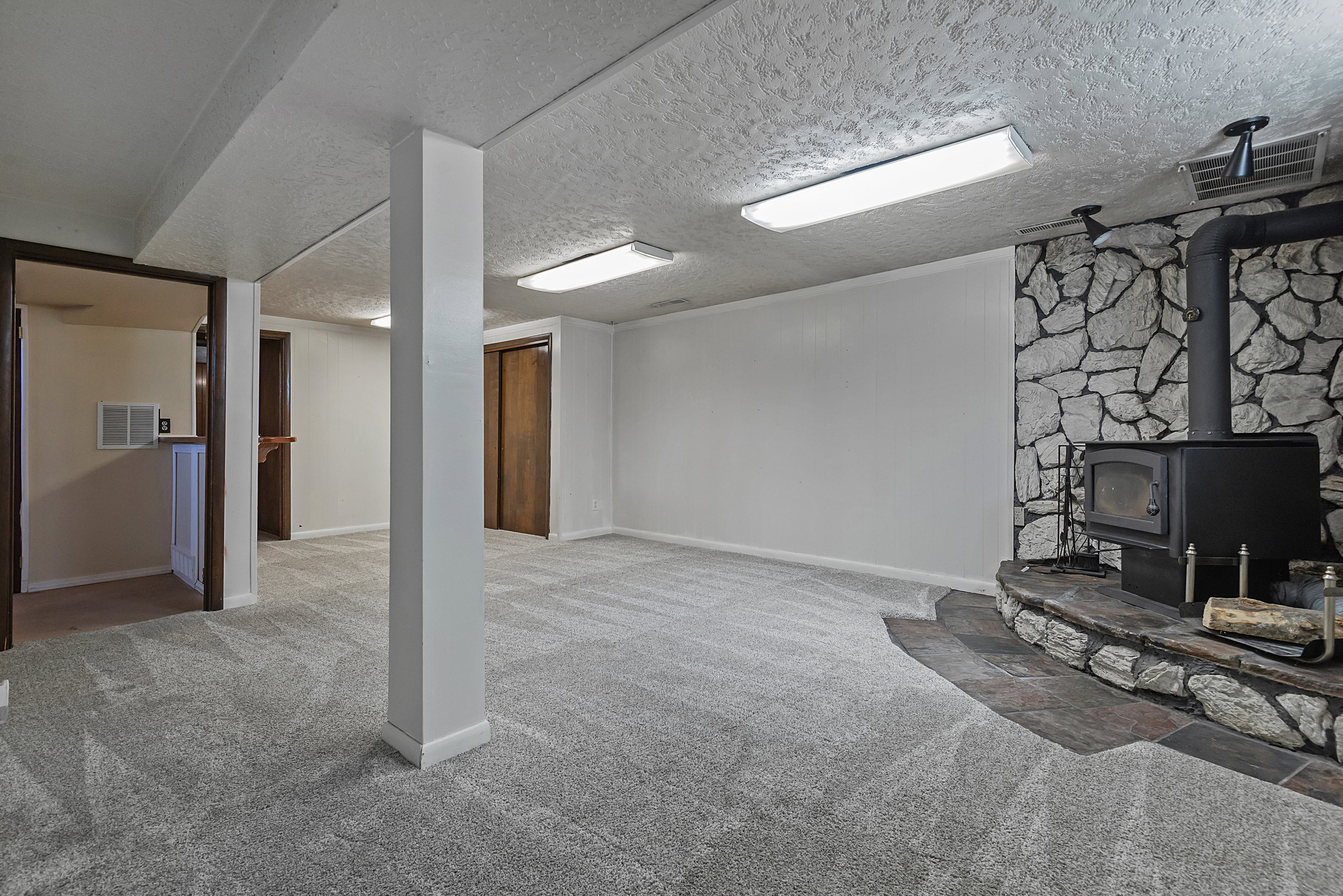 Expansive carpeted area featuring a stone accent wall with a built-in wood-burning stove and hearth