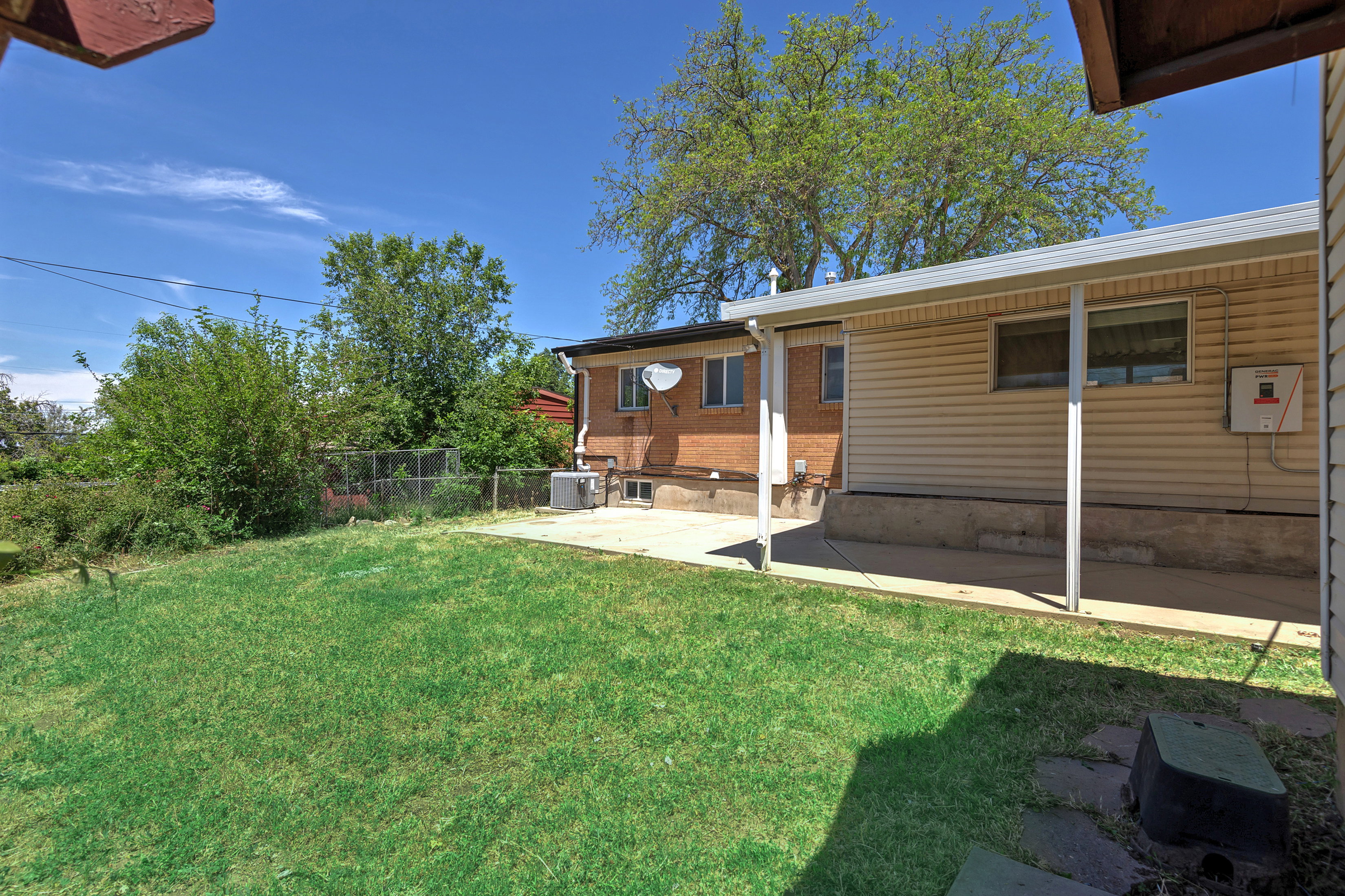 Expansive lawn area with a covered patio featuring a light-colored roof supported by white posts