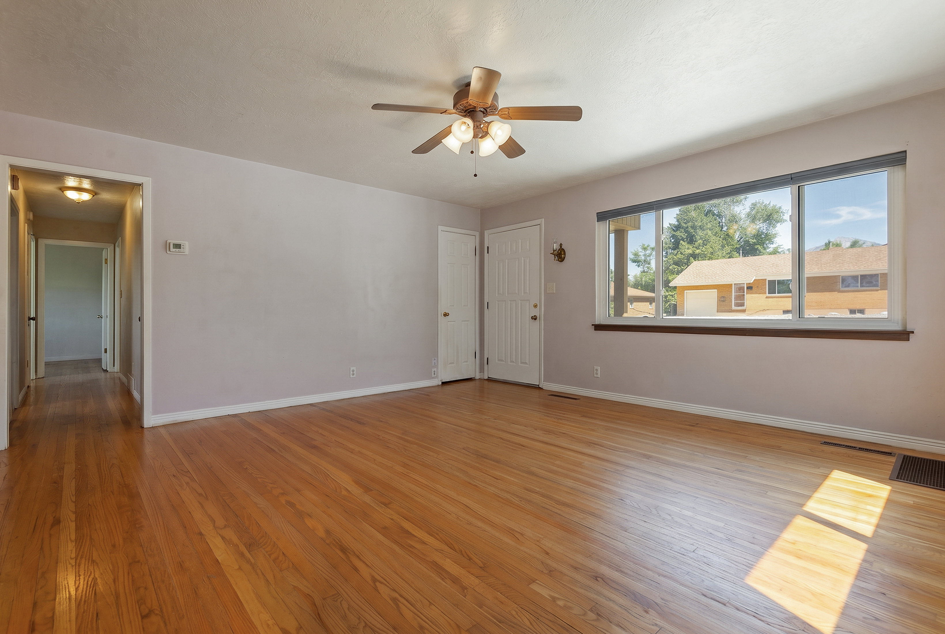 Bright living space featuring hardwood flooring, a ceiling fan with integrated lighting, and a large picture window