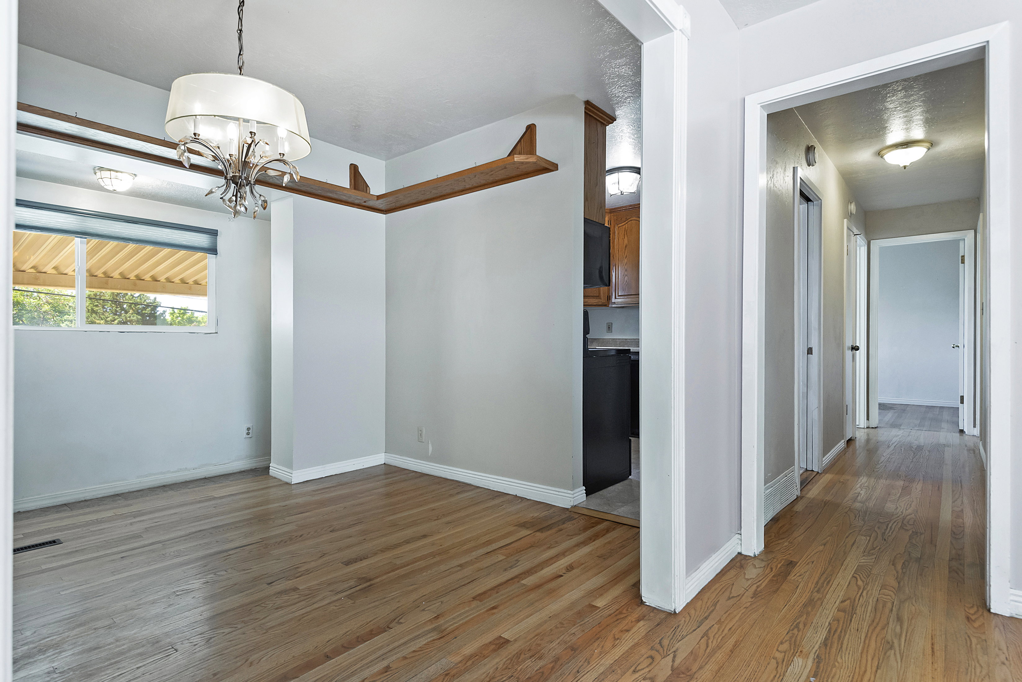 Hardwood flooring extends throughout this interior space featuring a decorative chandelier and a window with a roller shade