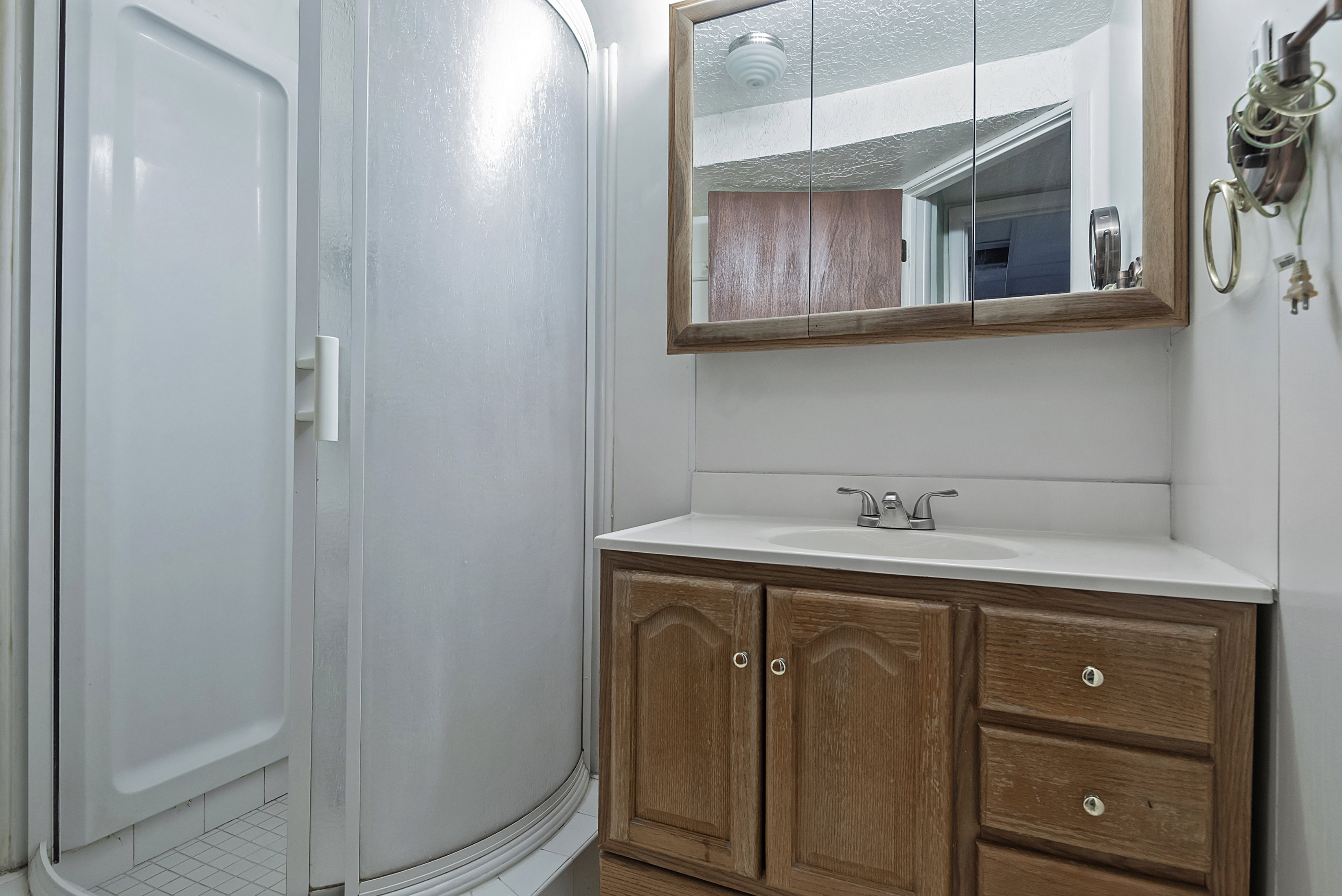 Three-panel medicine cabinet over a wood-finish vanity with a white countertop and integrated sink