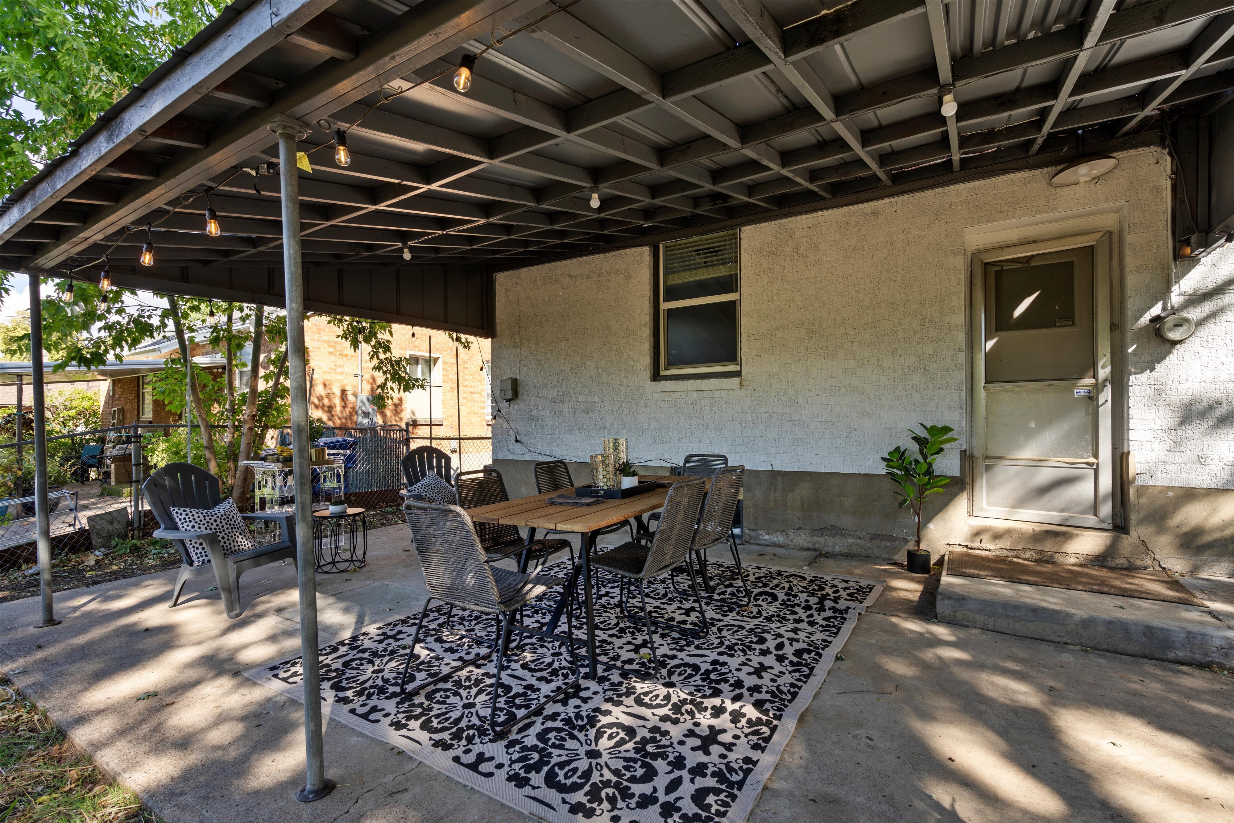 Covered concrete patio featuring string lighting, a rear entry door, and a window opening to the exterior
