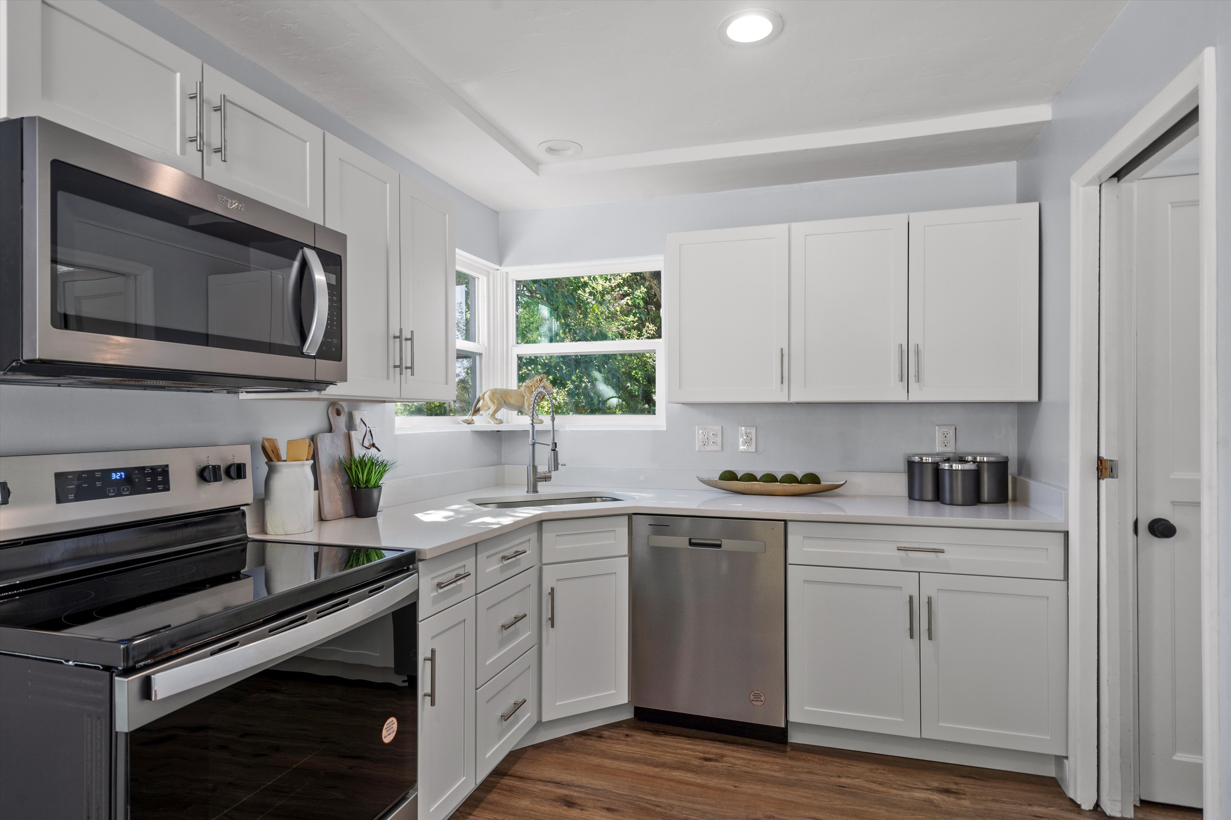 Modern kitchen featuring white shaker cabinetry, stainless steel appliances, light-toned countertops, wood-finish flooring, and a corner window