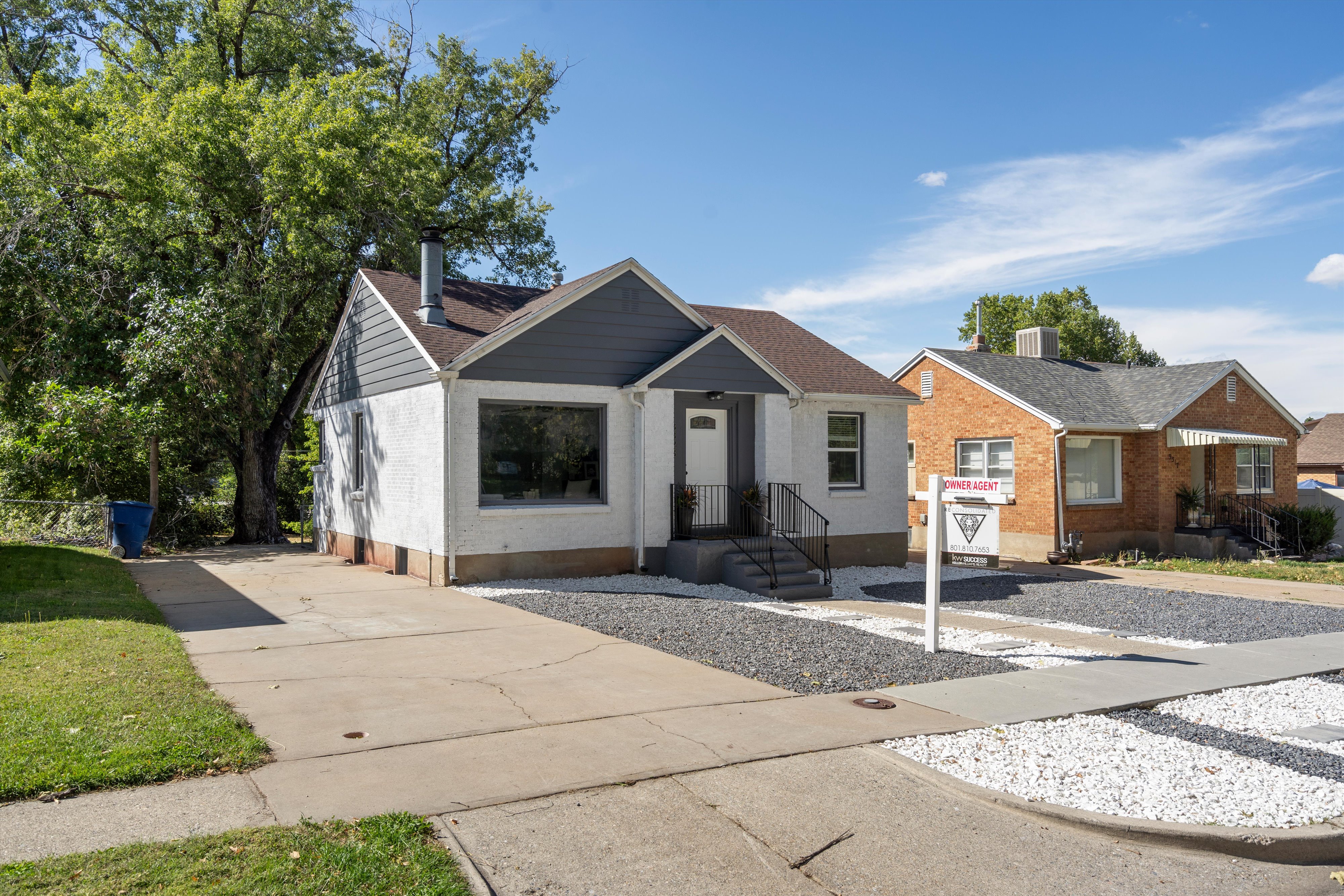 White stucco exterior with dark gray siding accents and a brown shingle roof