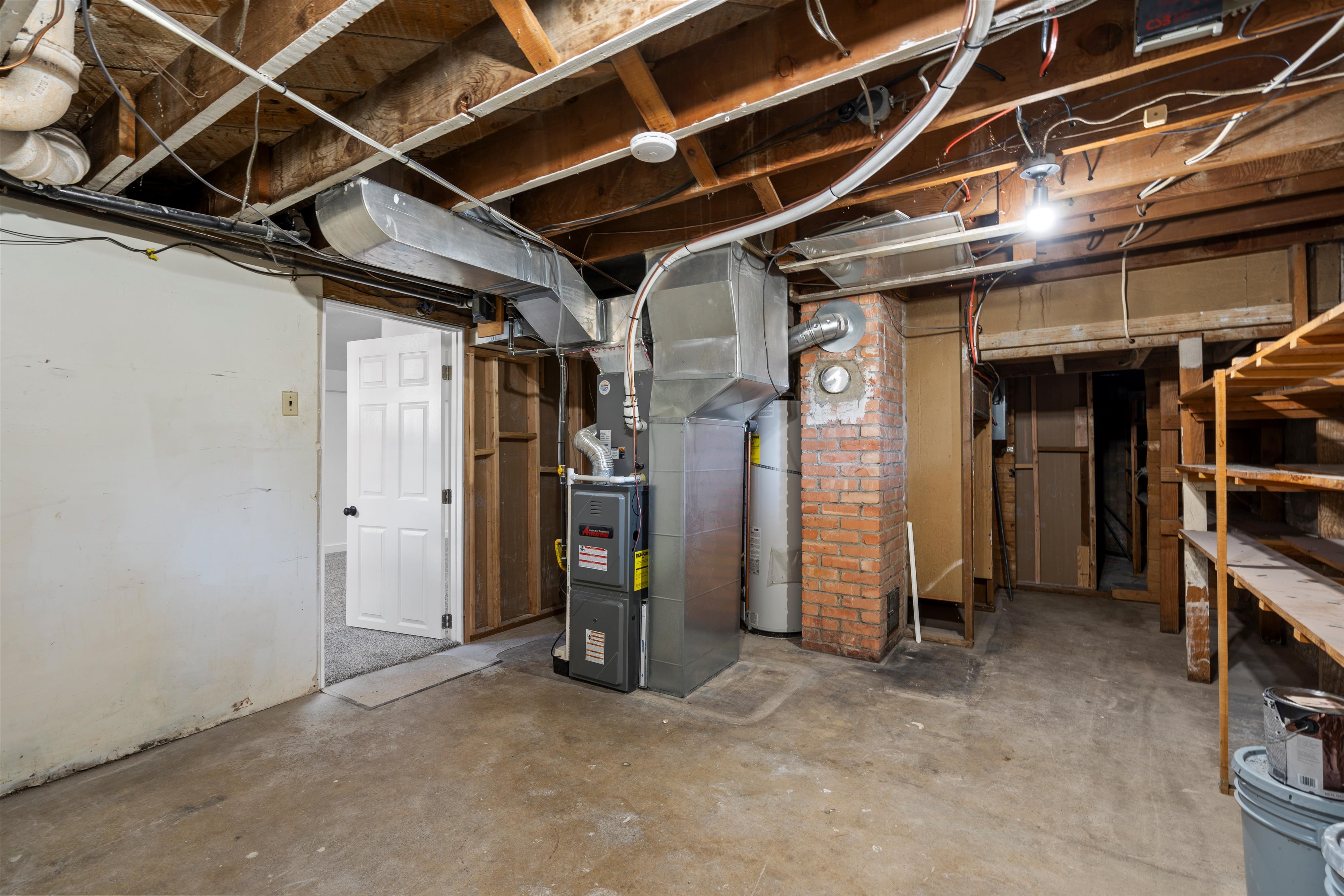 Unfinished basement area featuring exposed ceiling joists, concrete flooring, and an exposed brick column