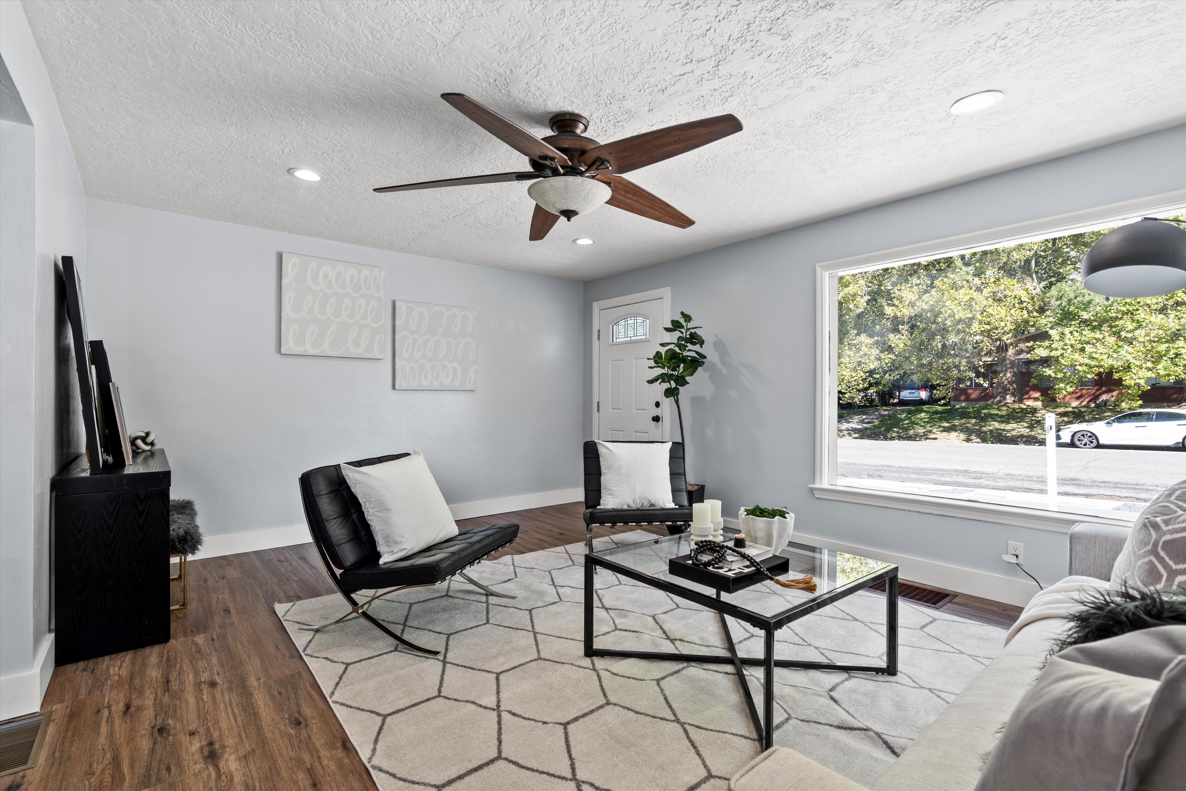 Spacious living area featuring wood-finish flooring, light blue walls, and a large picture window