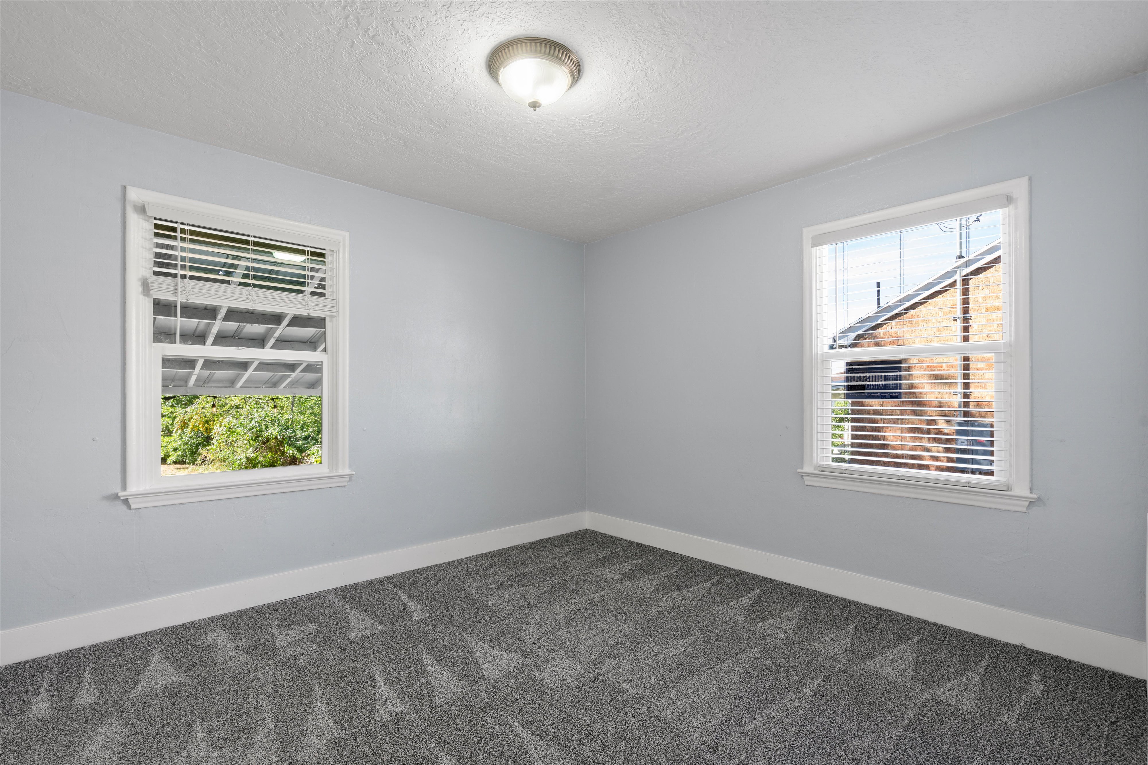 Room featuring two windows with white blinds, light blue painted walls, and patterned gray carpeting