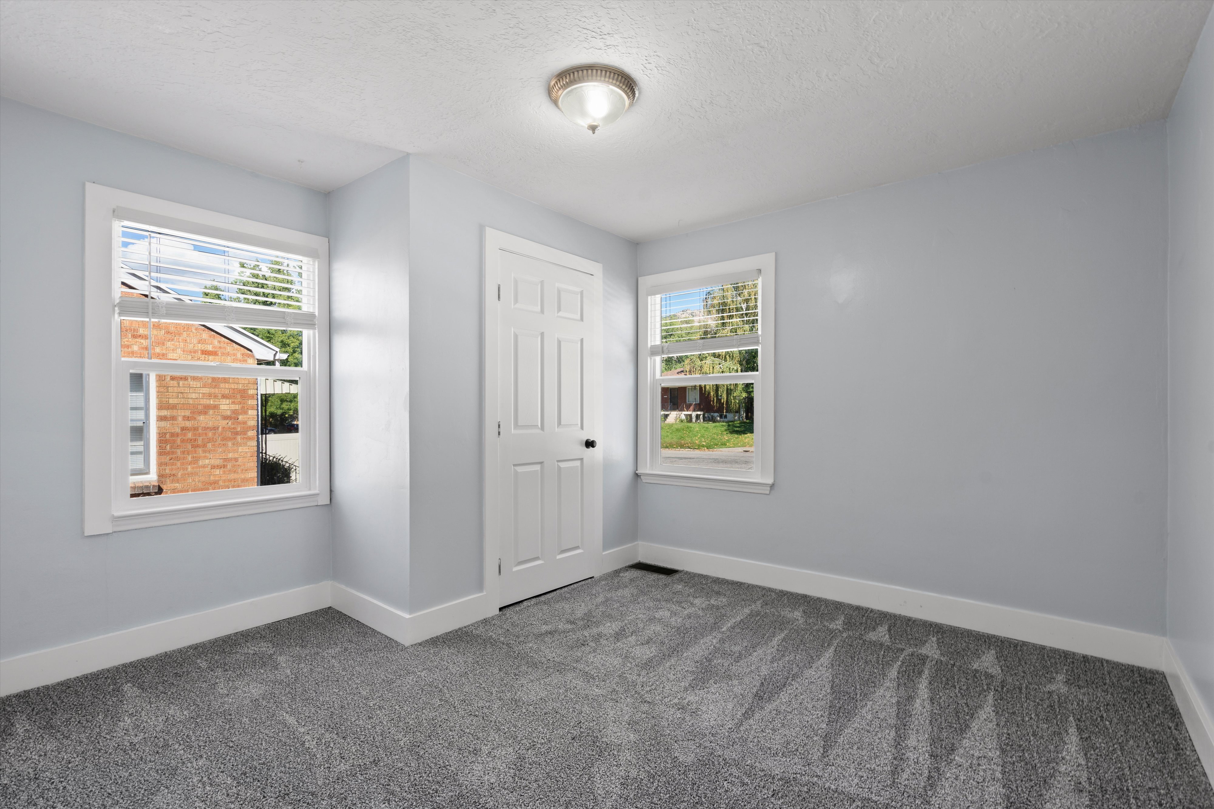 Room featuring two windows with white blinds, light gray wall paint, white trim, and gray patterned carpeting