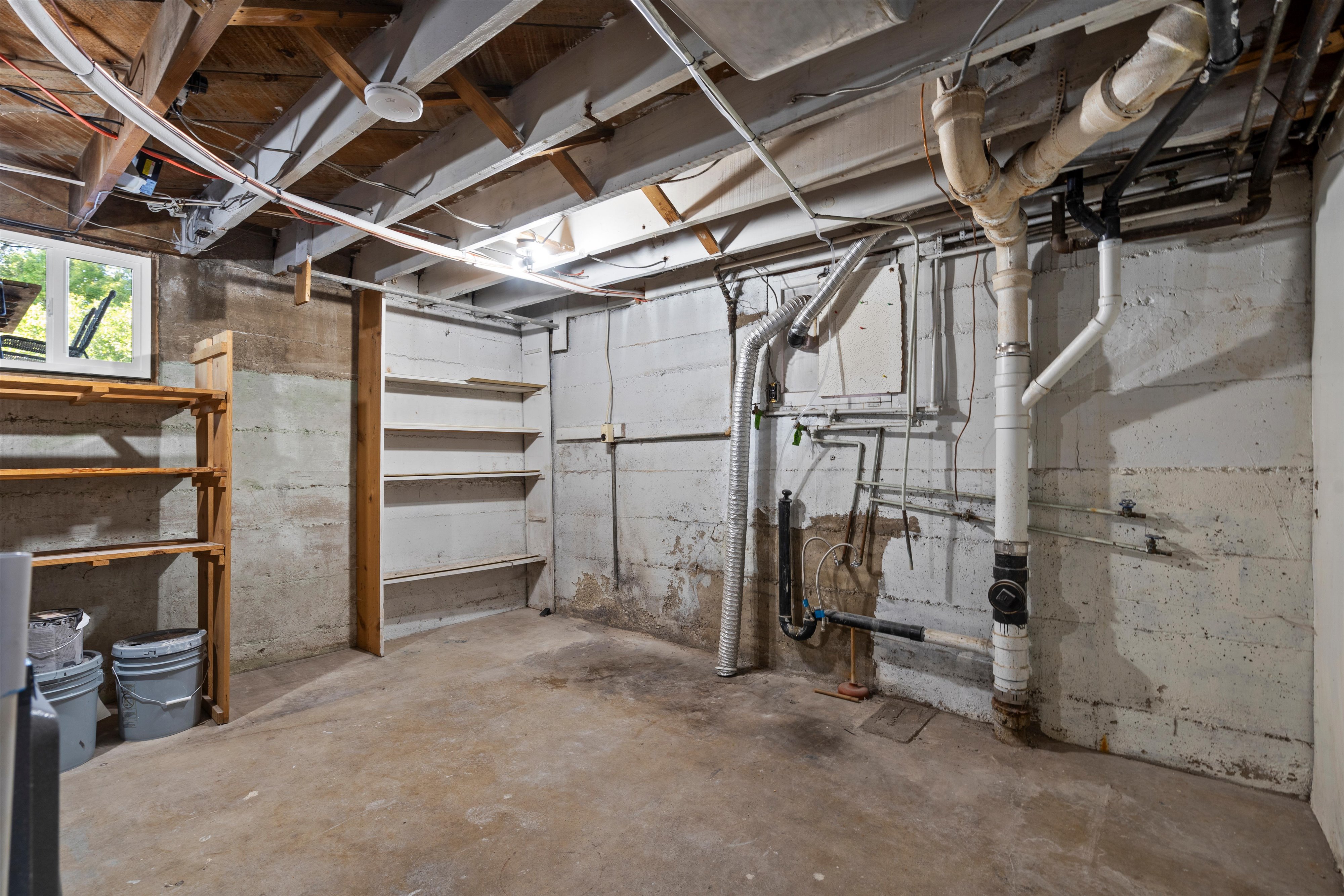 Concrete basement featuring exposed joists and plumbing