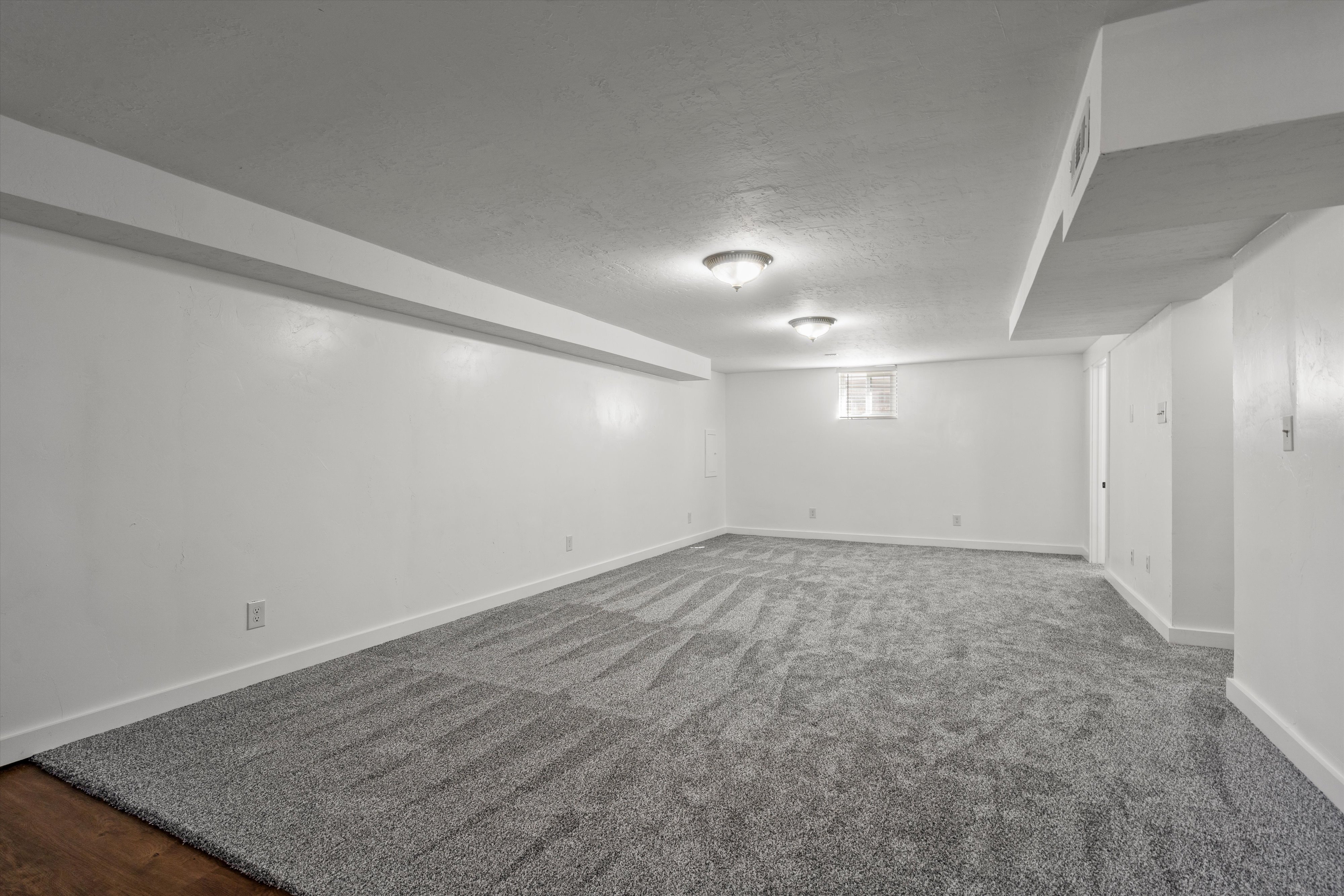 Spacious room featuring new patterned carpet flooring, recessed ceiling lighting, a window providing natural light, white painted walls, and white trim molding