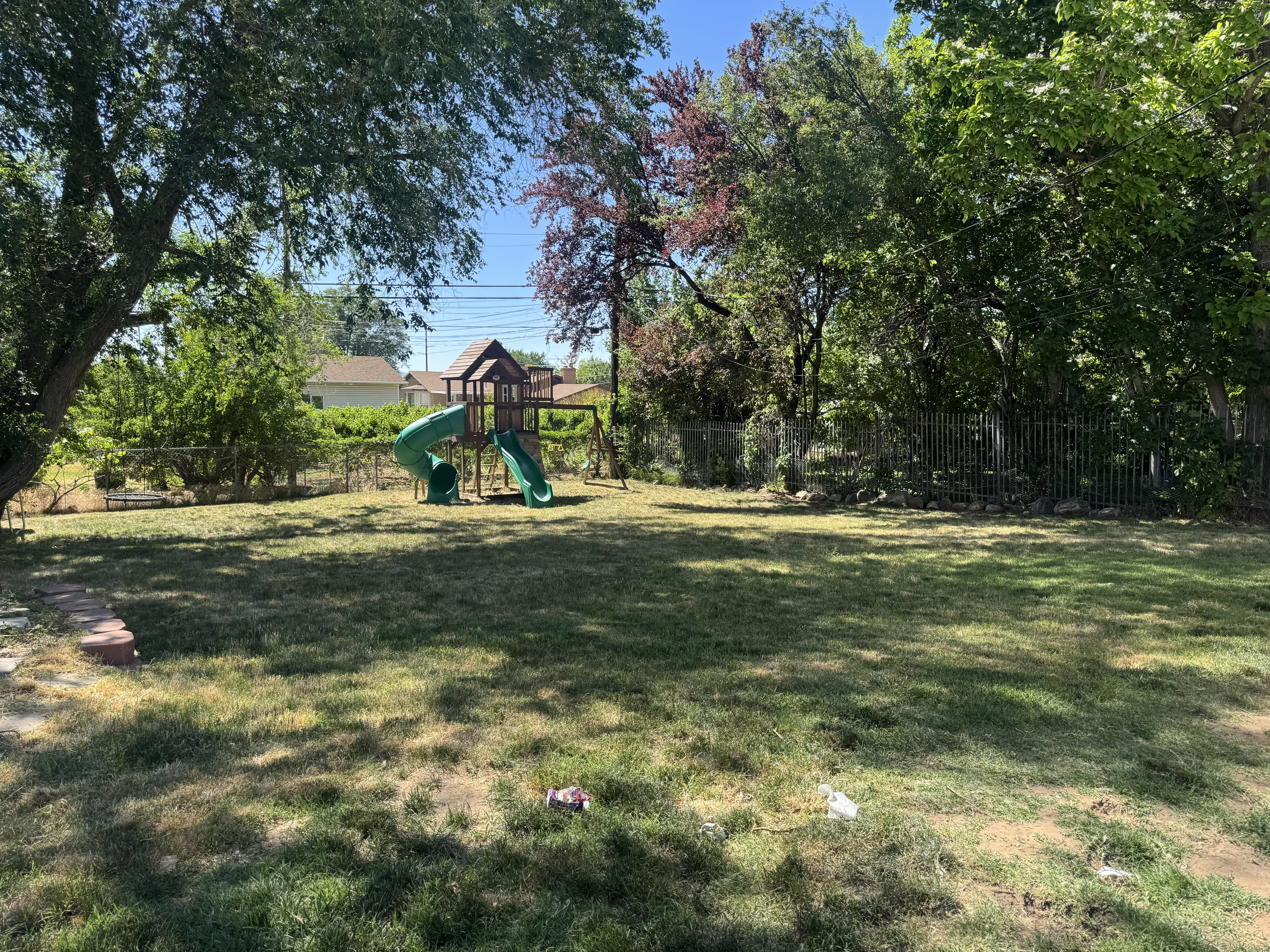 Expansive backyard featuring mature trees, a chain-link fence, and a swing set with two slides