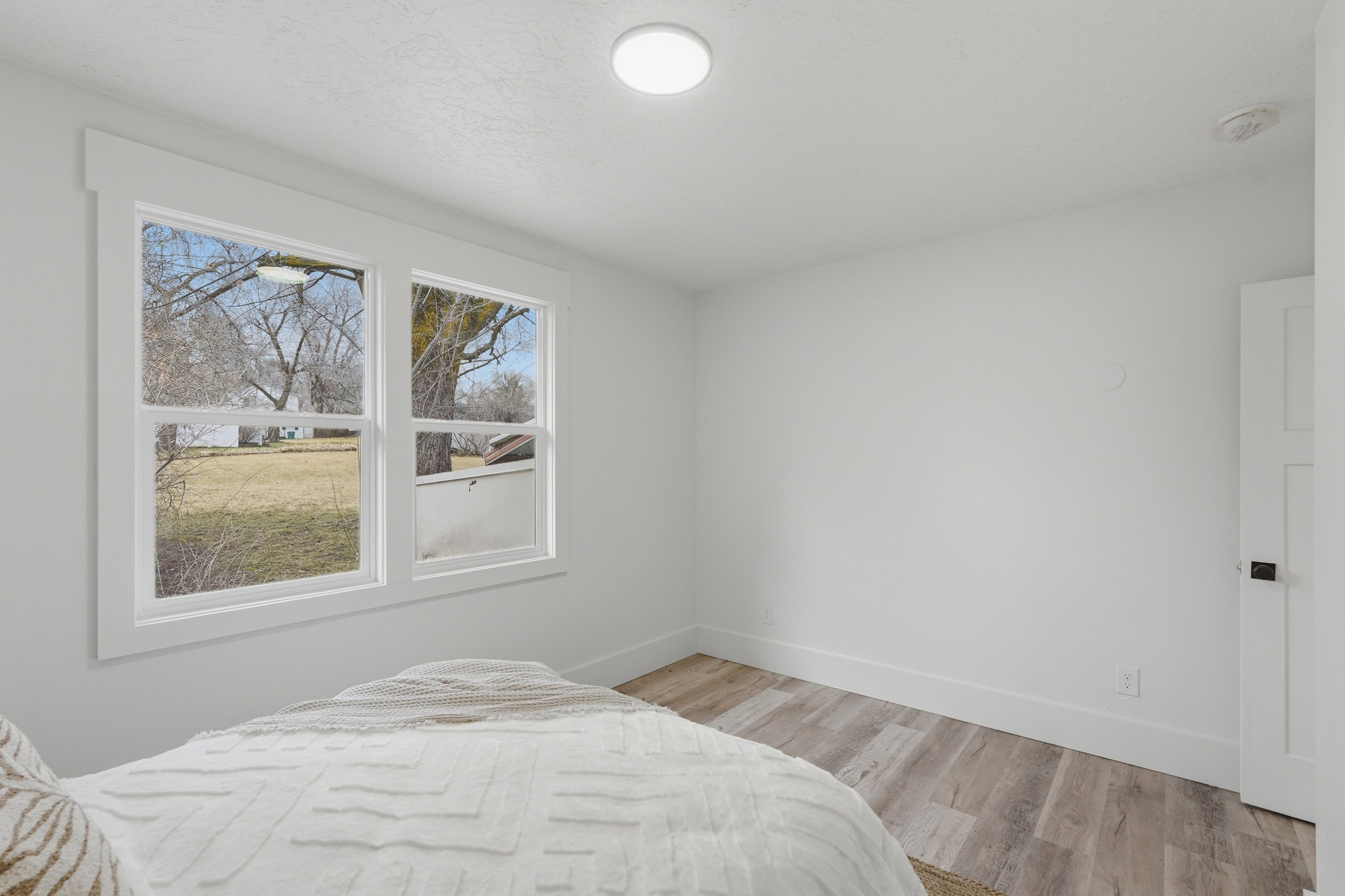 Room featuring dual windows with white trim, wood-finish flooring, white walls, and a flush-mount ceiling light