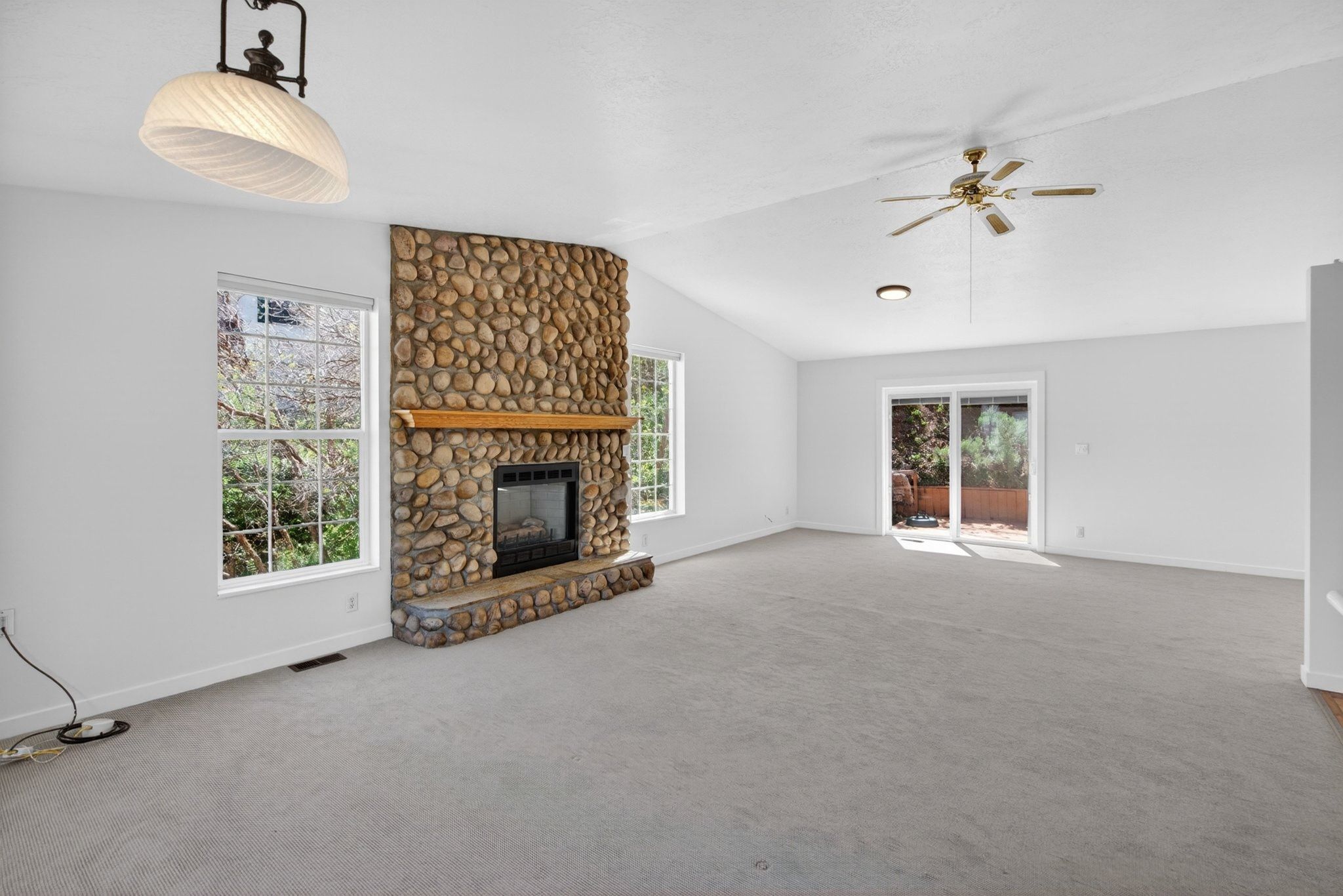 Spacious interior featuring a stone-faced fireplace with a wood mantle, vaulted ceiling, and light gray carpeting
