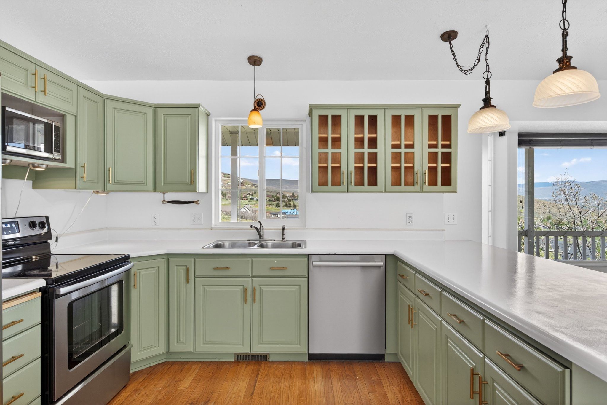 Kitchen featuring light green cabinetry with gold hardware, white countertops, and wood-finish flooring