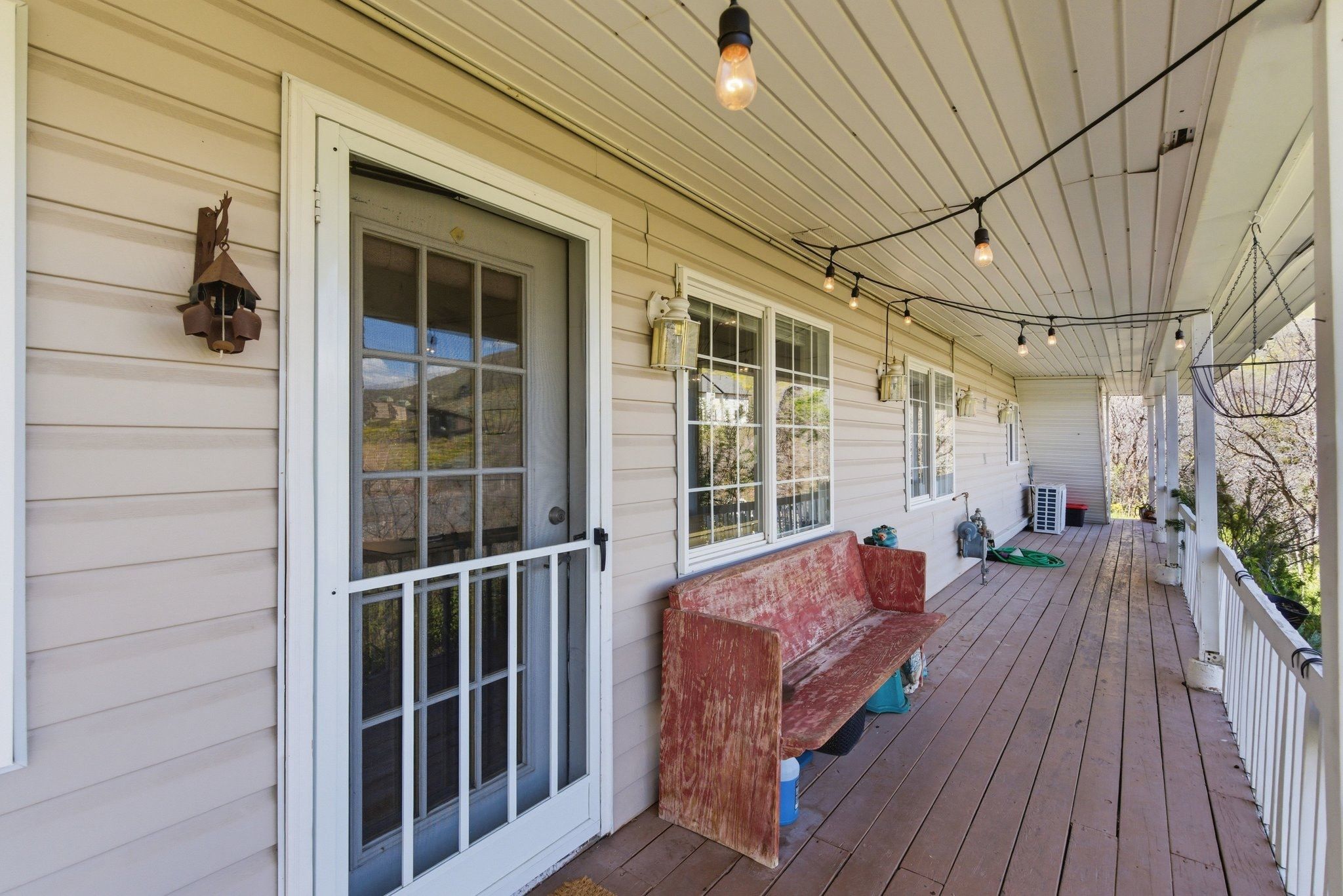 Expansive covered porch featuring wood-finish decking, horizontal siding, multiple windows, and a glass-paneled screen door
