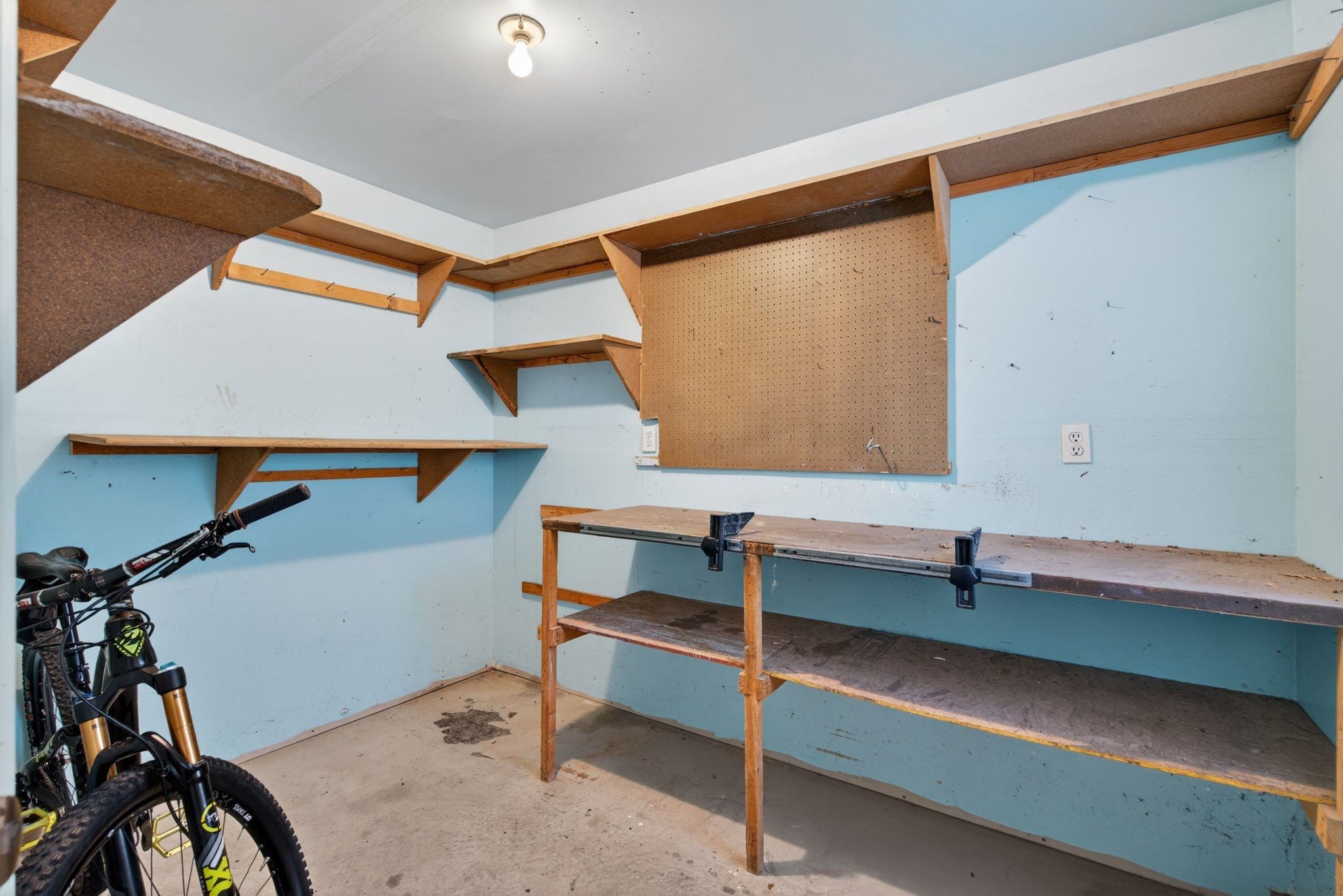 Utility space featuring light blue walls, built-in shelving, pegboard, and a workbench with integrated vises