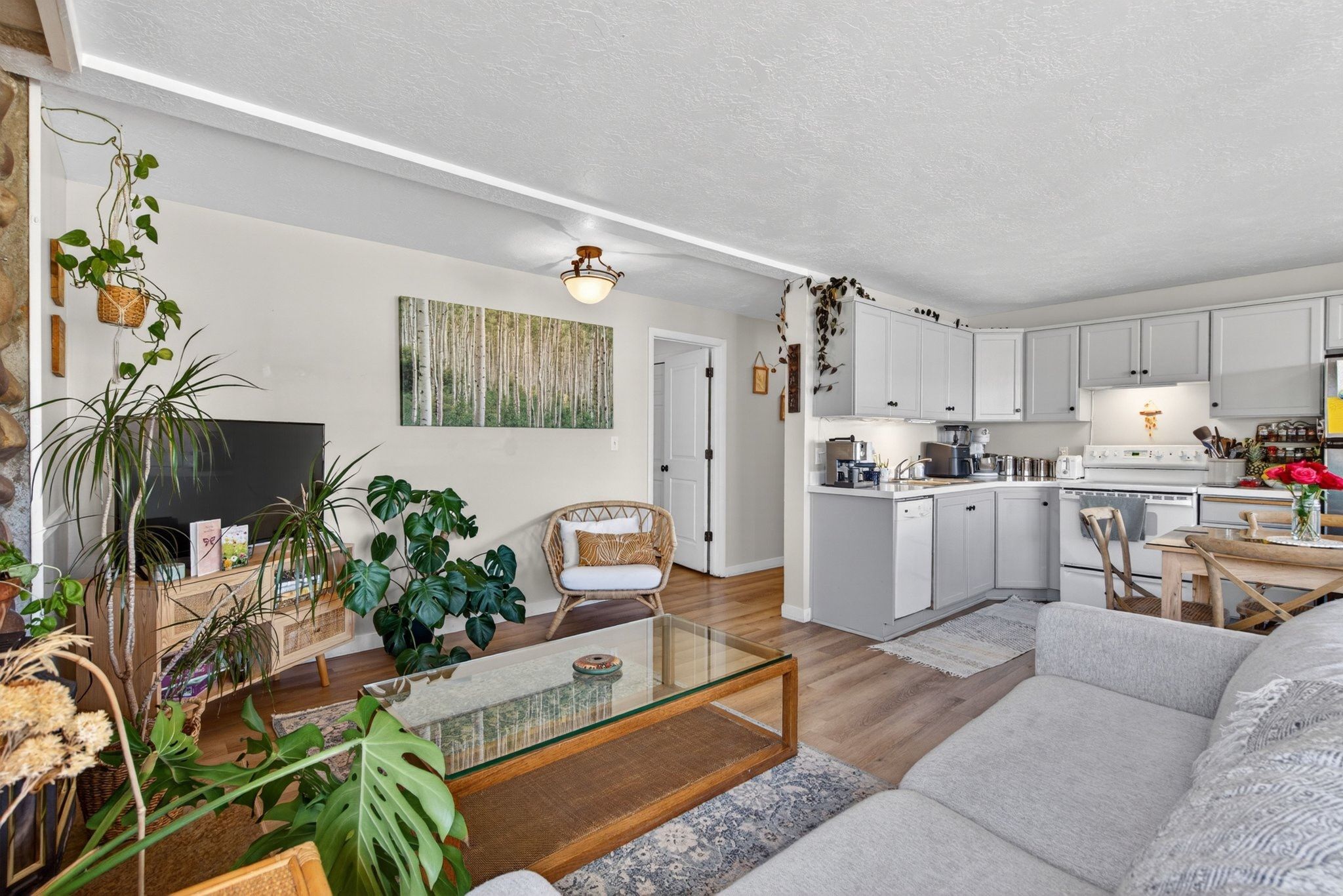 Open-concept living space featuring wood-finish flooring, a stone accent wall, and a kitchen with light gray cabinetry, built-in appliances, and recessed lighting
