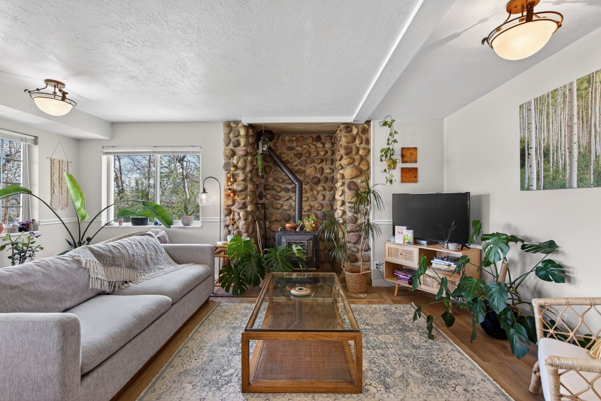 Living area featuring a stone accent wall with a built-in wood-burning stove, large windows, wood-finish flooring, and a recessed ceiling light fixture