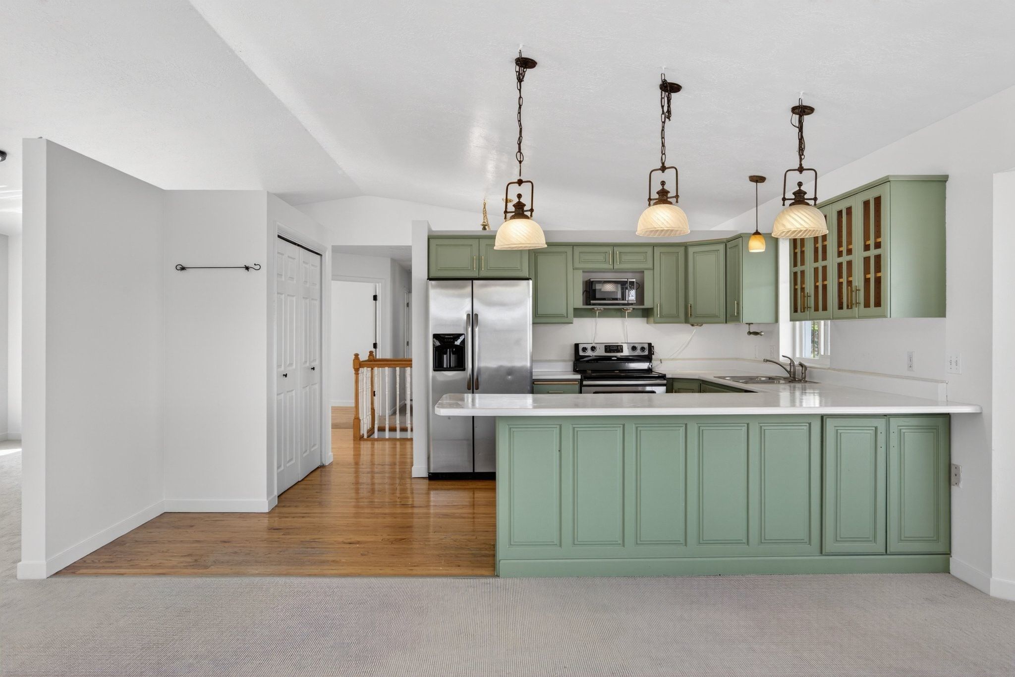 Kitchen featuring mint green cabinetry, stainless steel appliances, a white countertop, and three pendant lights