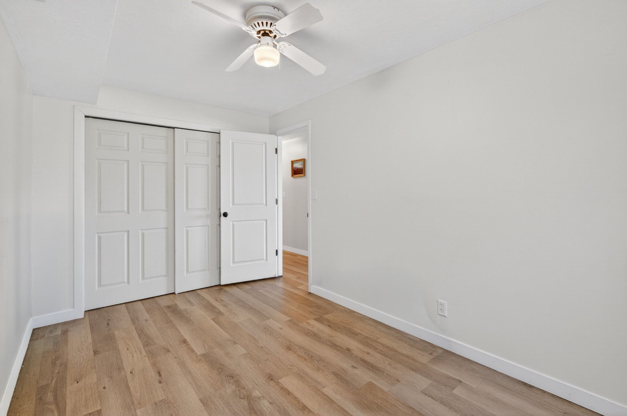 Room featuring wood-finish flooring, a ceiling fan with integrated lighting, and white walls
