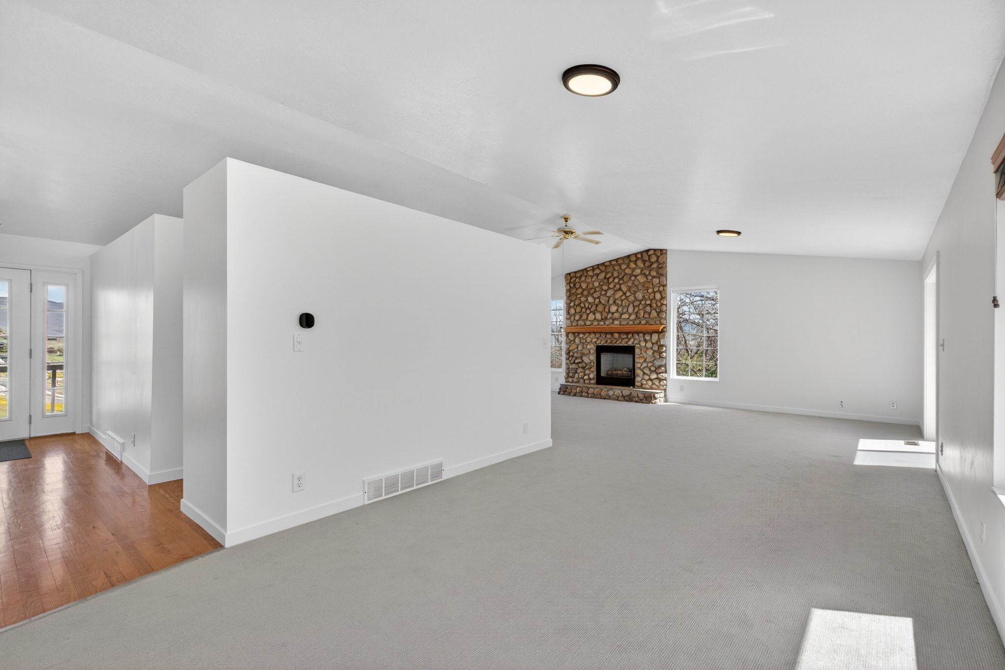 Spacious living area featuring a stone fireplace, light-toned carpeting, and white walls