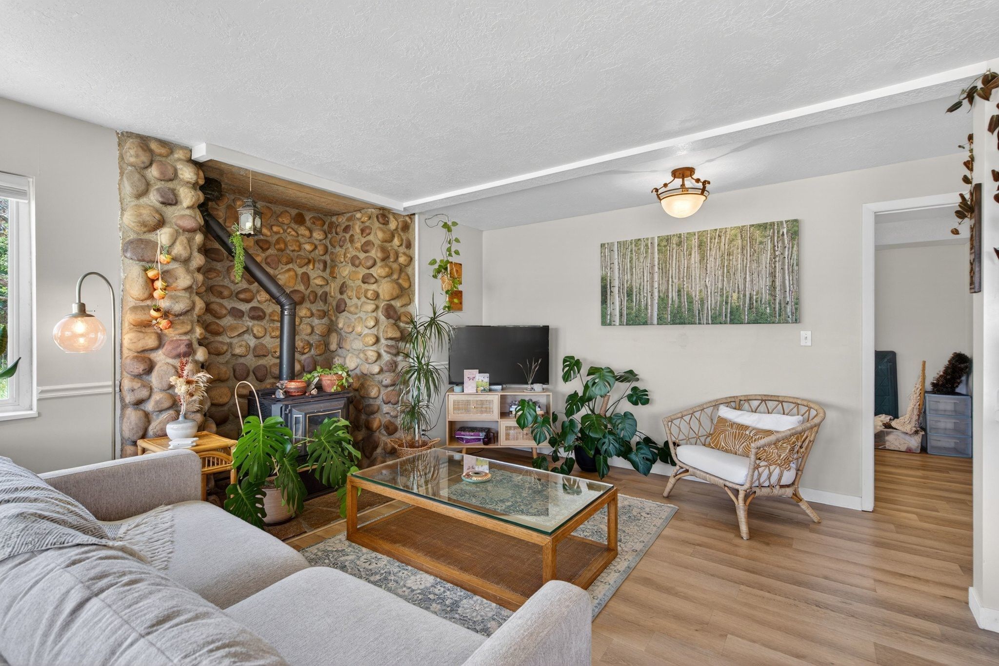 Living area featuring a stone accent wall with a built-in wood-burning stove, light-toned wood-finish flooring, white trim, and a ceiling-mounted light fixture
