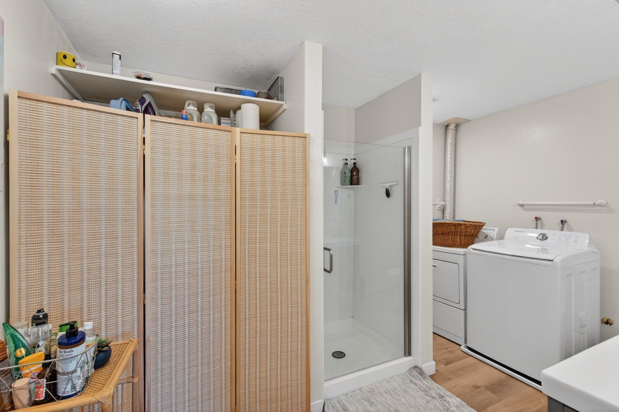 Three-panel room divider with shelving, a glass-enclosed shower, wood-finish flooring, and a dedicated laundry area with hookups