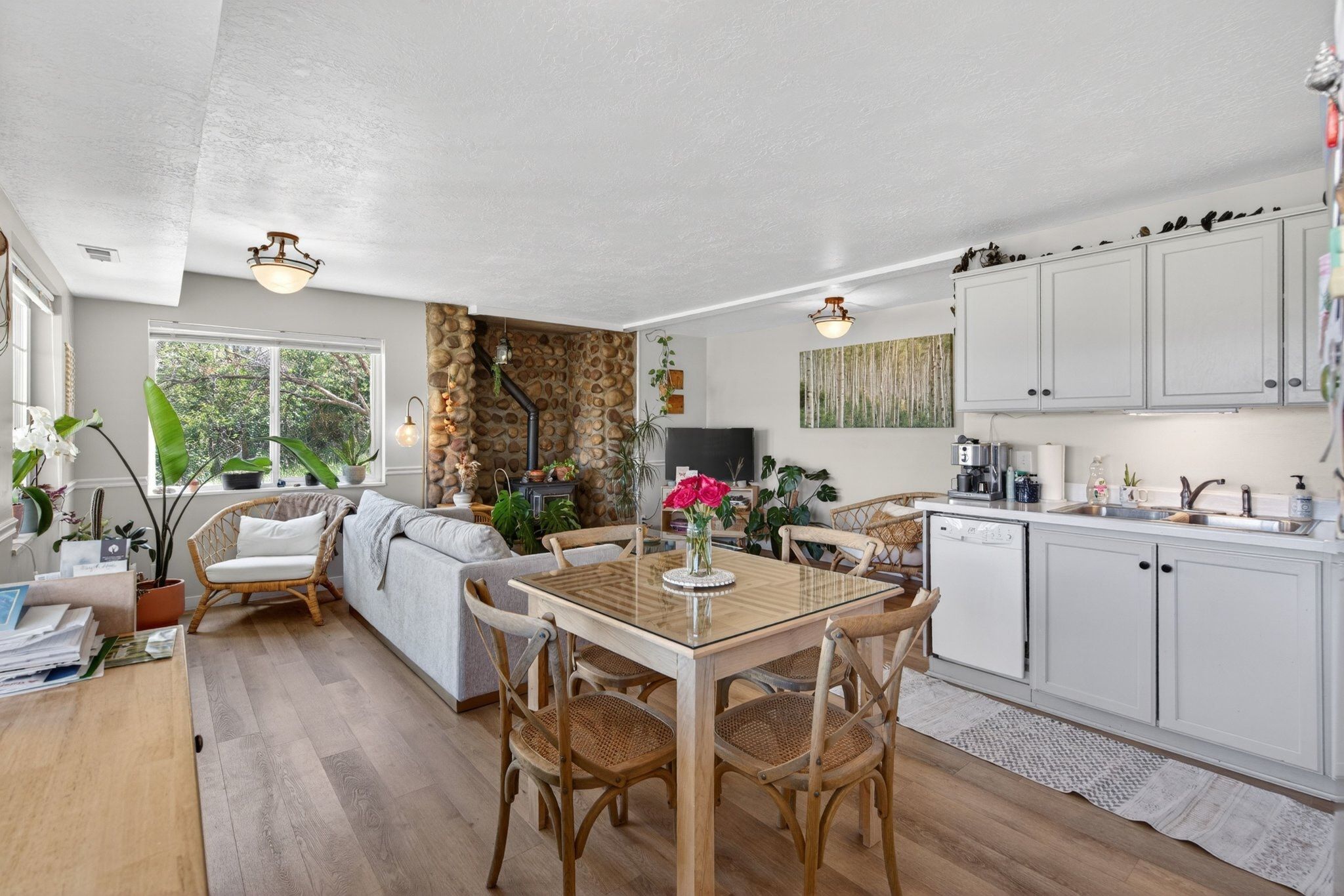 Open-concept living area featuring wood-finish flooring, a stone-accented wall, and a built-in kitchen area with light cabinetry and a white countertop