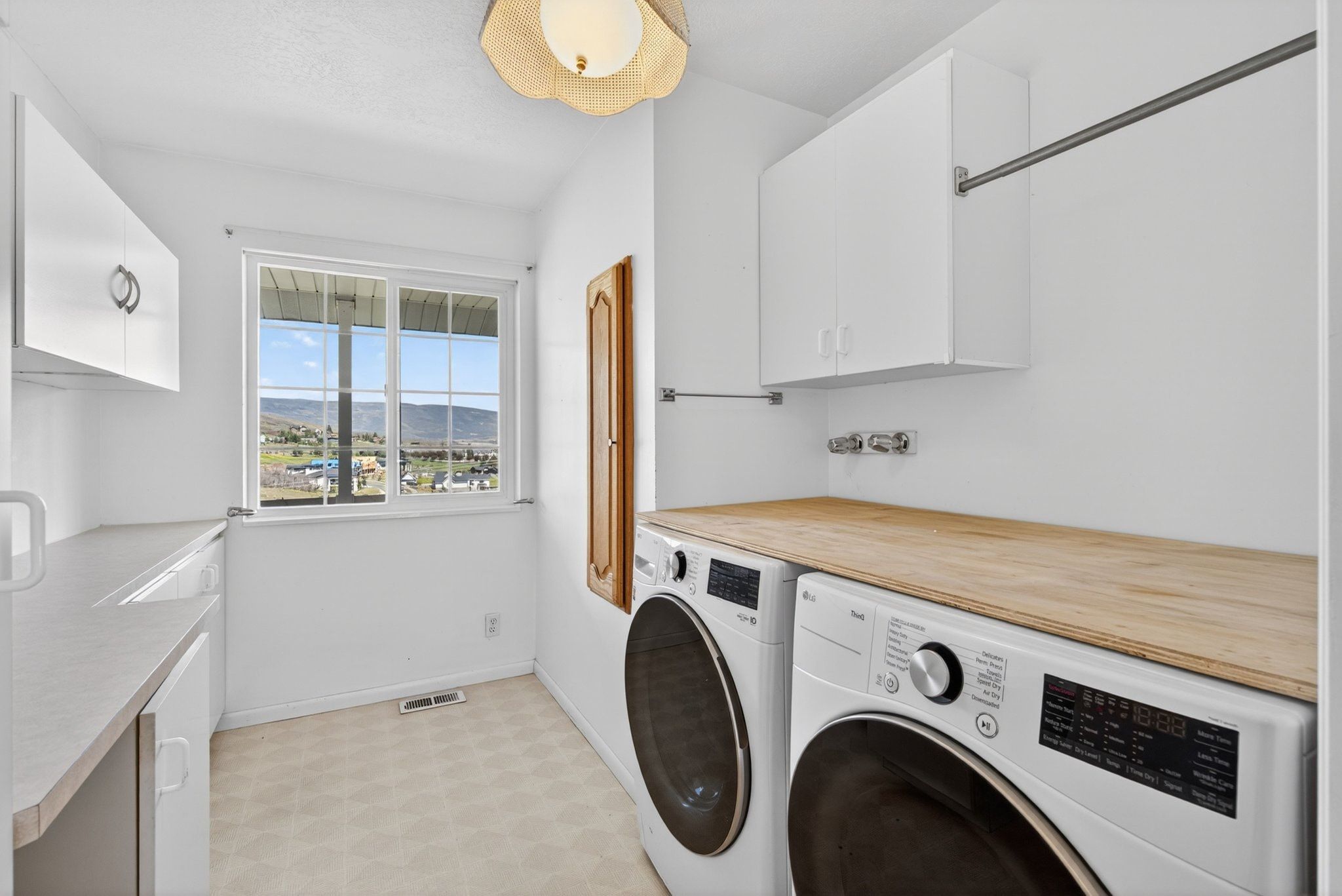 Dedicated laundry area featuring white cabinetry, wood-finish countertop, and a window framing distant hills