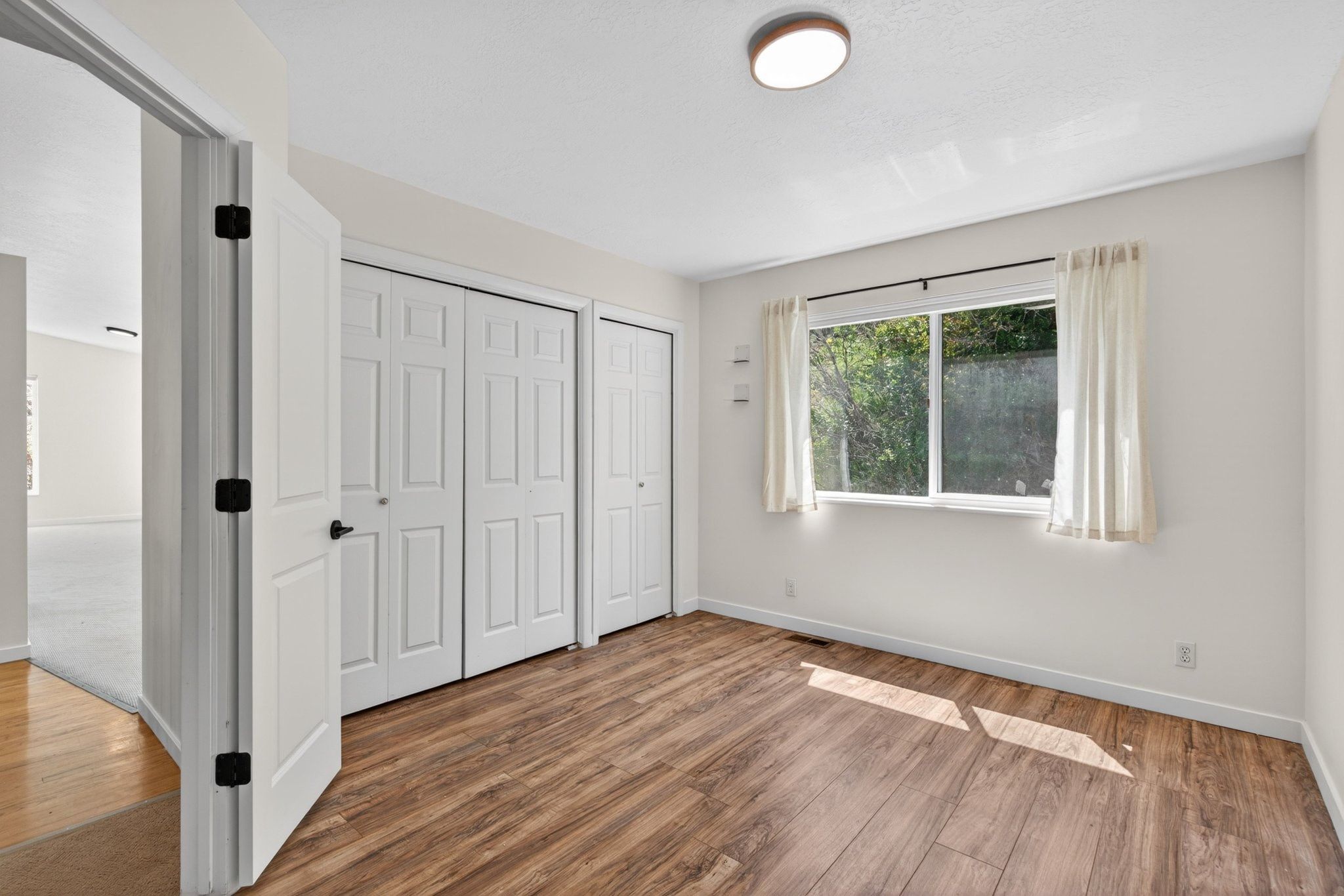Room featuring wood-finish flooring, a large window, a ceiling-mounted light fixture, and two bi-fold door closets