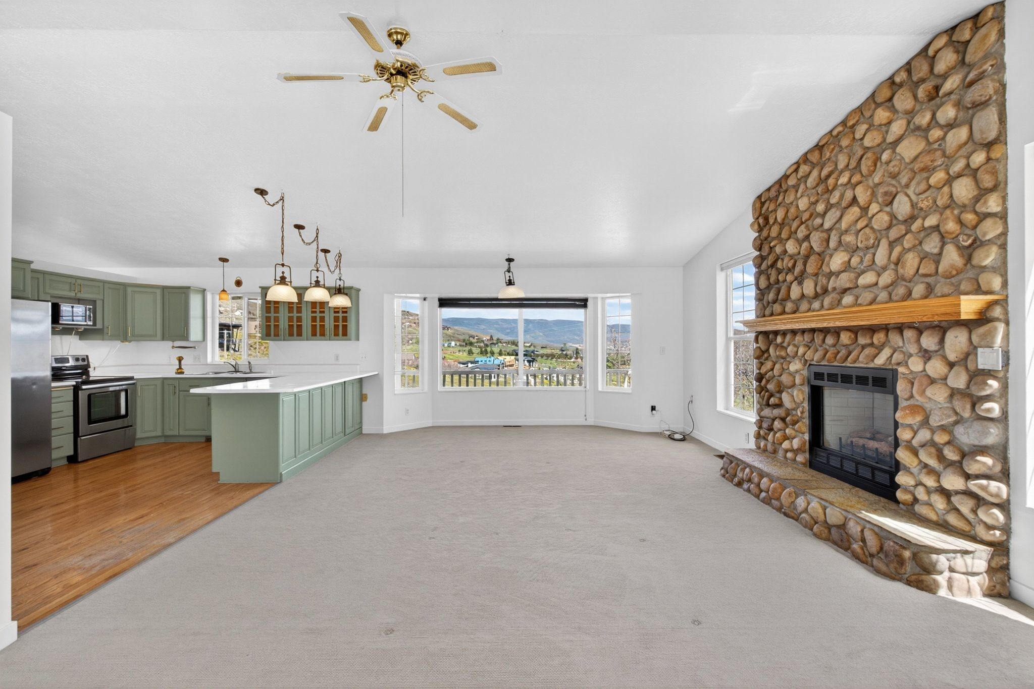 Spacious open-concept living area featuring a stone fireplace with a wood mantle, a ceiling fan, and carpeted flooring
