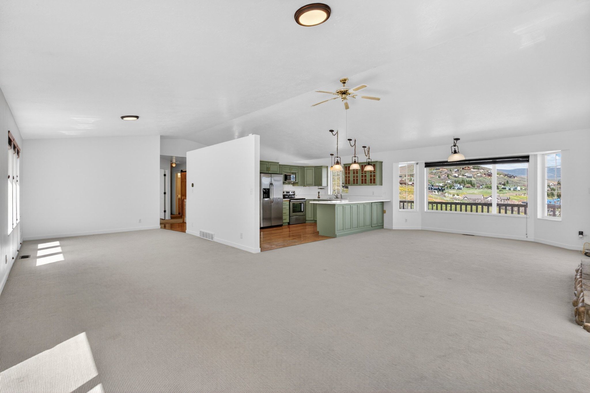 Expansive great room featuring light-colored carpet flooring, white walls, and a ceiling fan