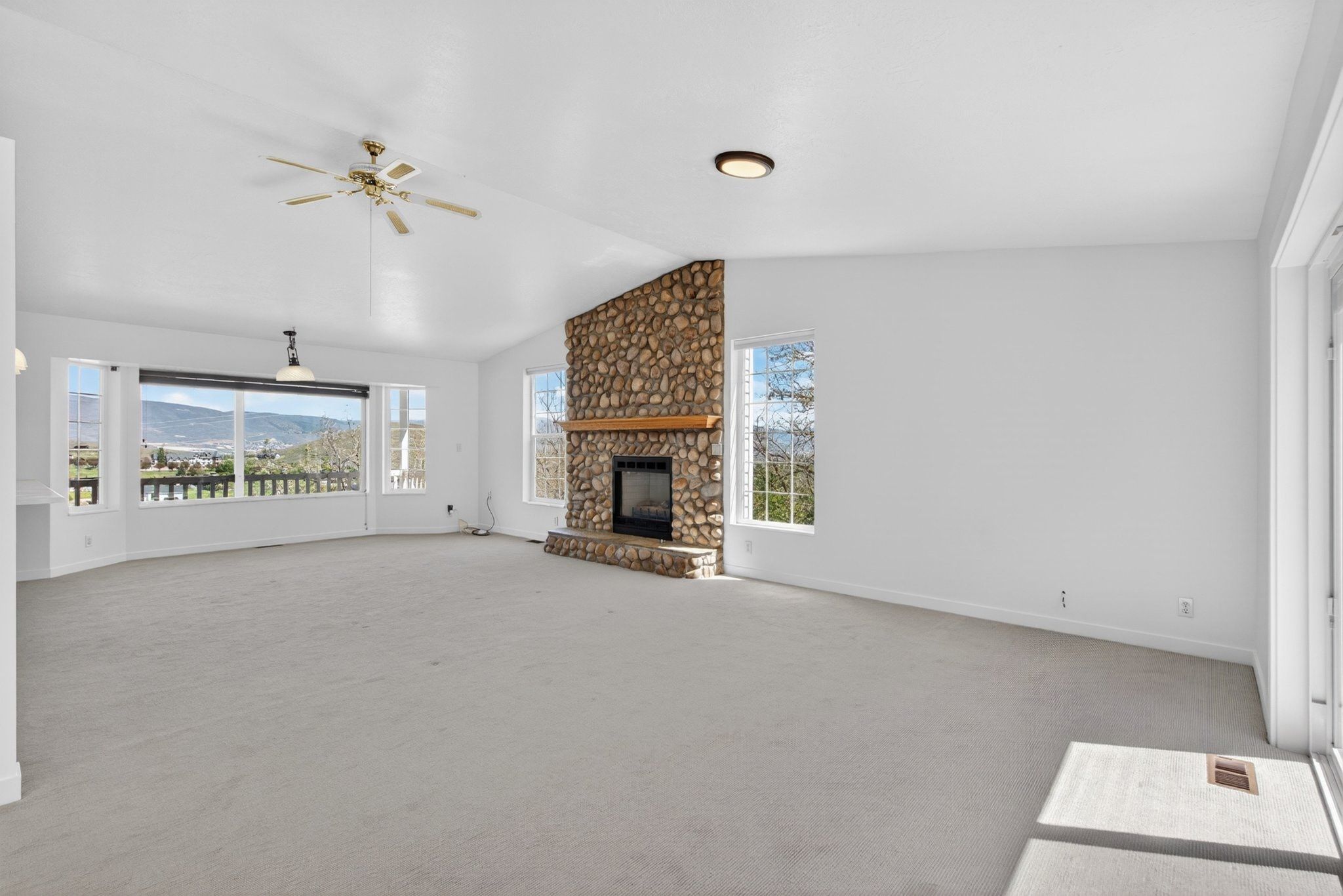 Spacious living area featuring a floor-to-ceiling stone fireplace, vaulted ceiling, and multiple windows