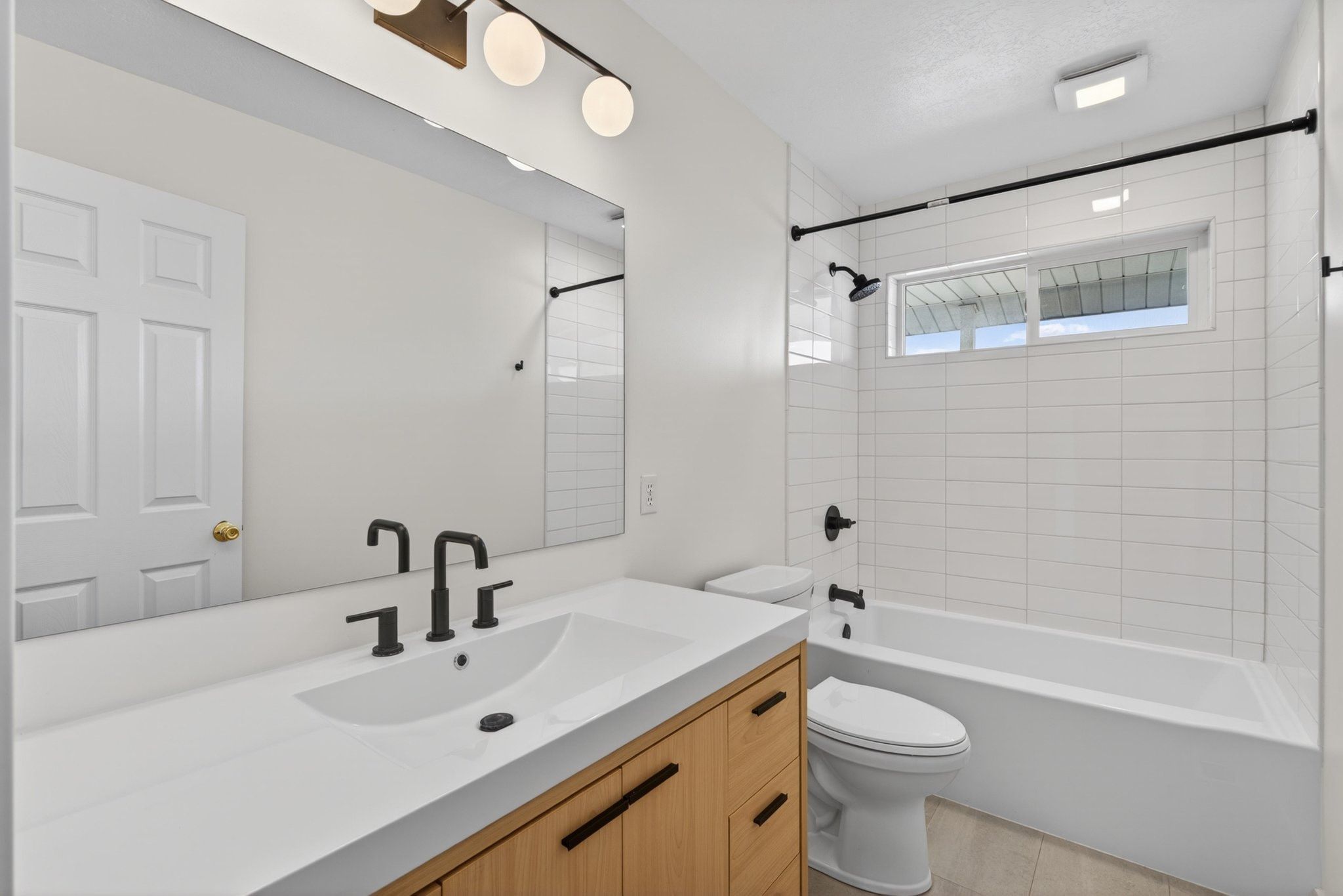 Bathroom featuring a wood-finish vanity with a white countertop and integrated sink, matte black fixtures, and a frameless mirror