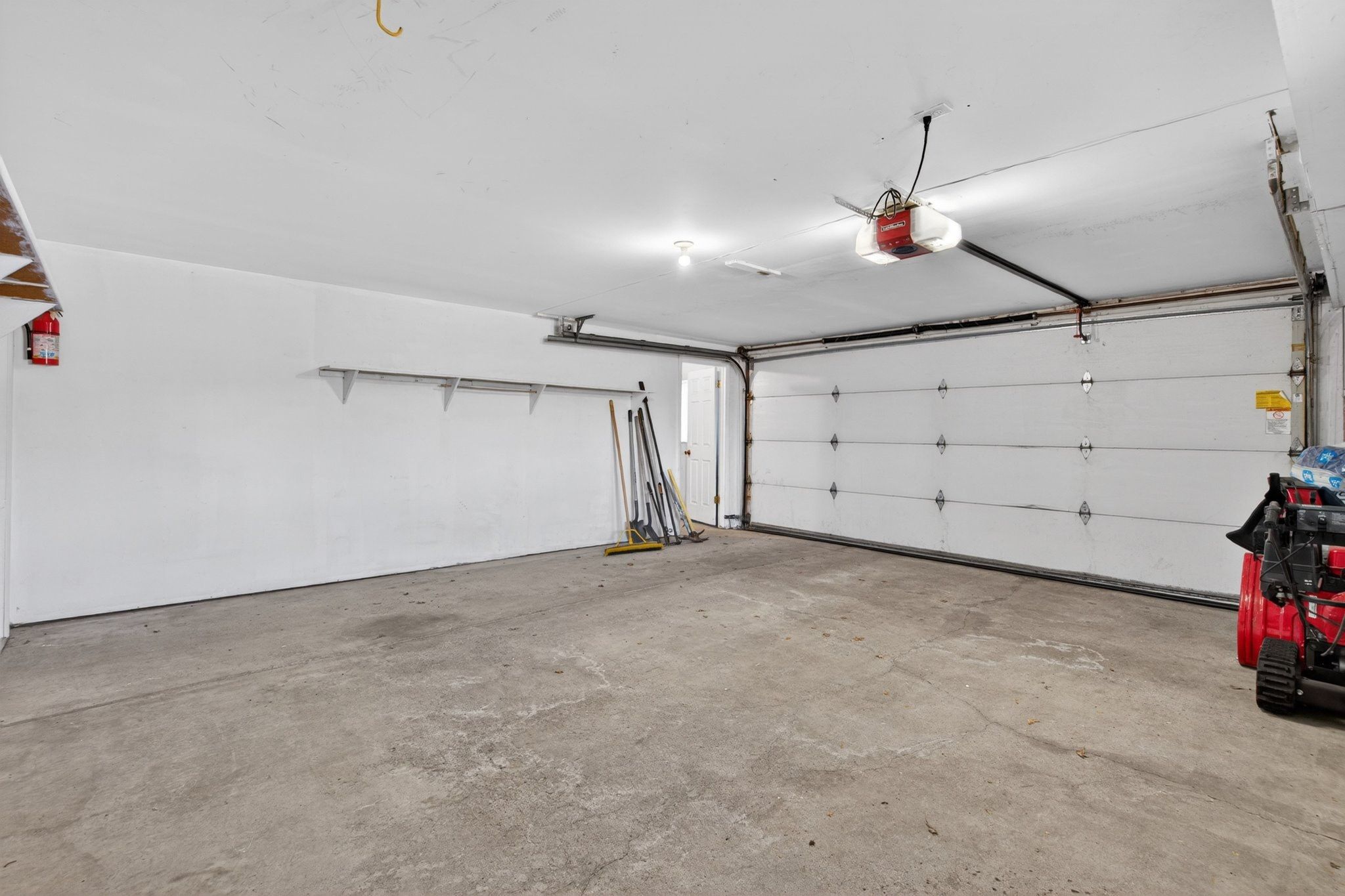 Spacious garage featuring a concrete floor, white walls, and a white paneled garage door with an automatic opener