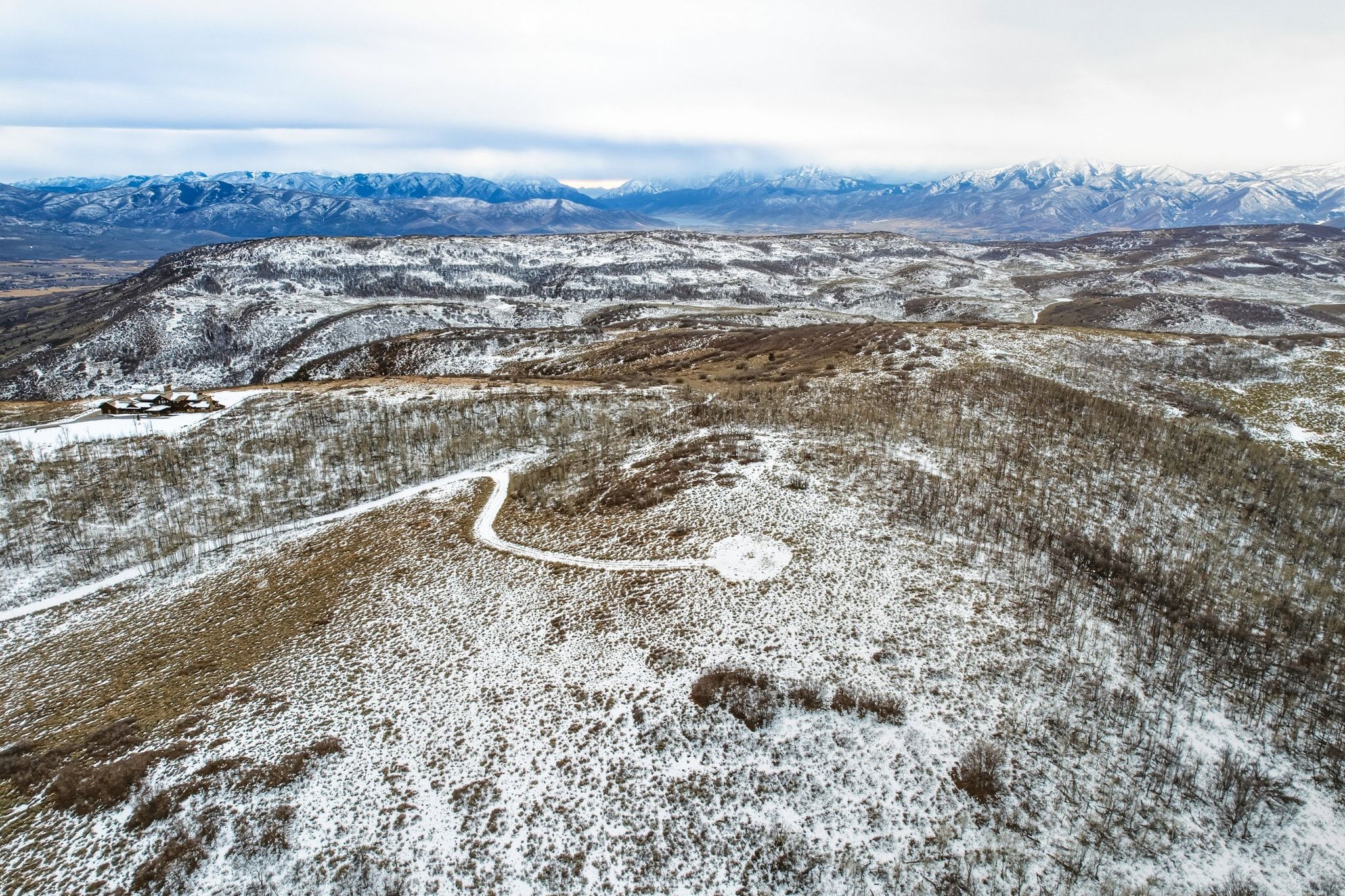 Expansive, snow-dusted landscape featuring distant mountain ranges and a winding access road
