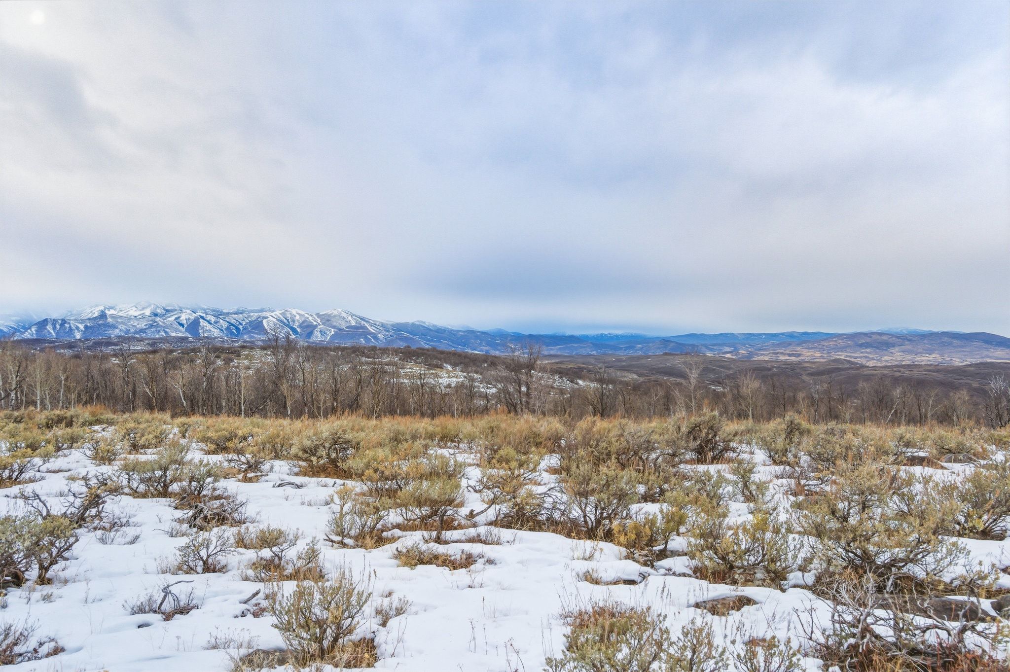 Expansive natural landscape featuring snow-dusted groundcover and distant mountain ranges