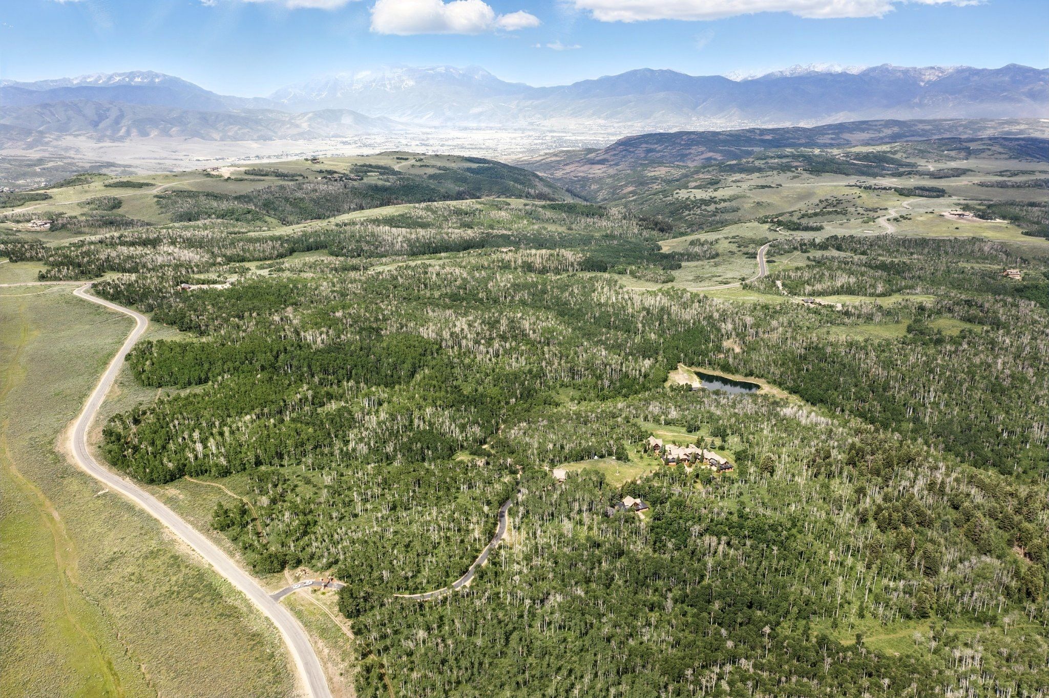 Expansive wooded landscape featuring a winding road, a small body of water, and distant mountains