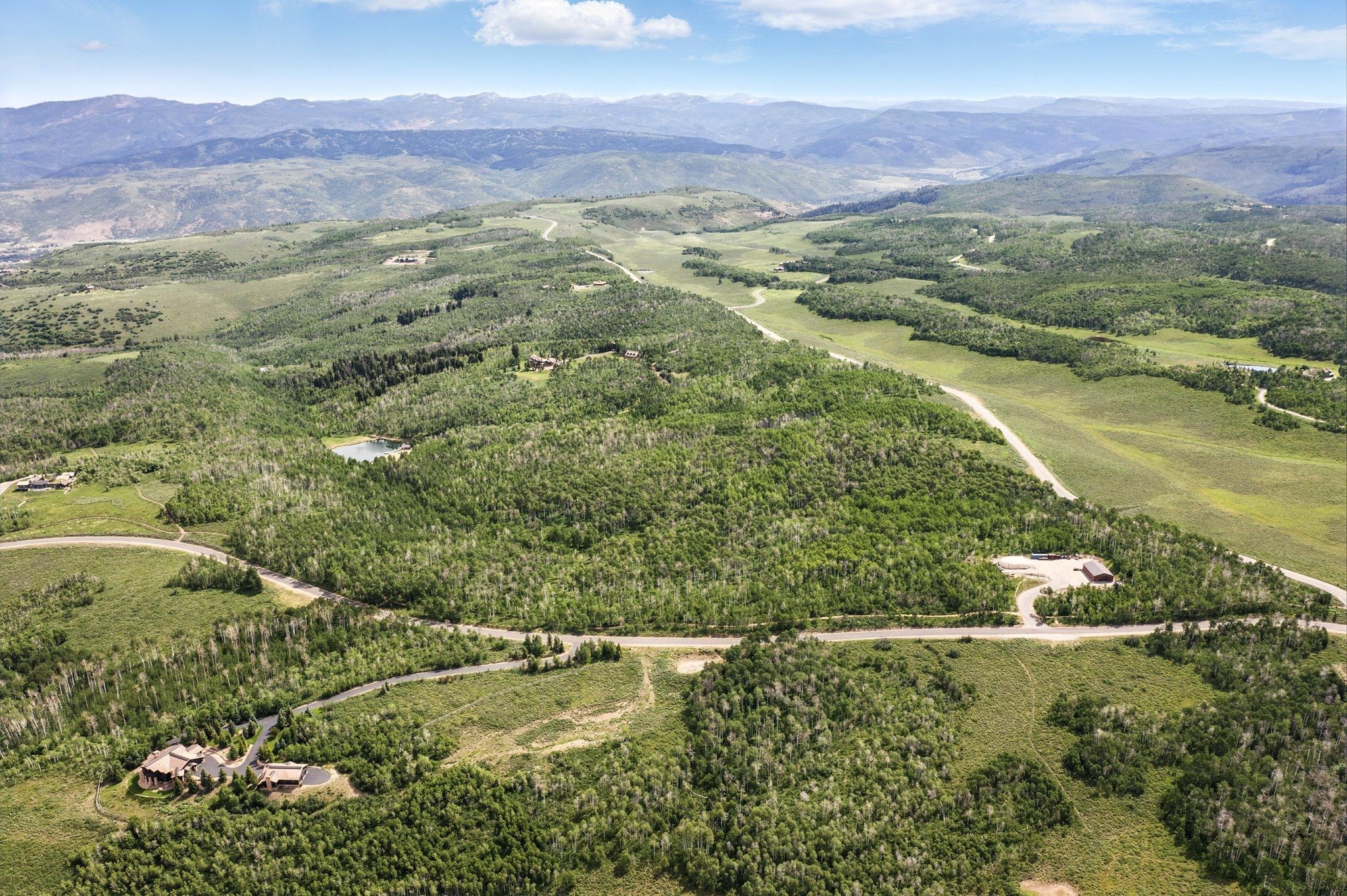 Expansive mountain landscape featuring varied terrain, a winding road, and scattered residential structures