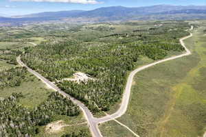 Expansive mountain property featuring significant tree coverage and clearings, a paved road network, and distant mountain ranges under a clear sky