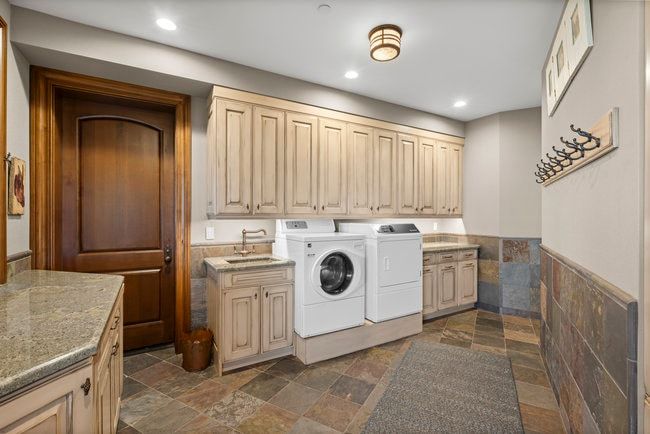Utility room featuring integrated washer and dryer, extensive upper and lower cabinetry, stone countertop surfaces, a utility sink with a bronze-finish faucet, and slate tile flooring