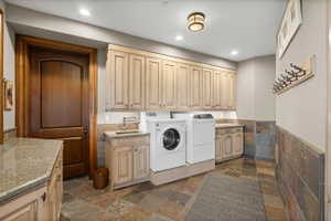 Utility room featuring integrated washer and dryer, extensive upper and lower cabinetry, stone countertop surfaces, a utility sink with a bronze-finish faucet, and slate tile flooring