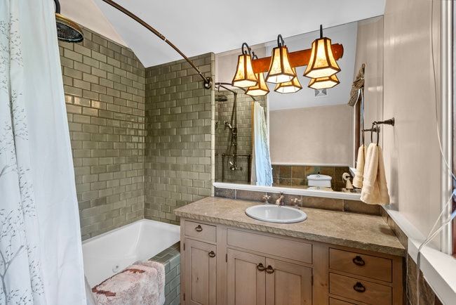 Bathroom featuring a tub/shower combination with subway tile surround, a single vanity with a stone-finish countertop, undermount sink, and wood-finish cabinetry