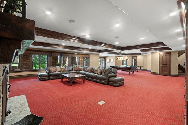 Spacious recreation room featuring red patterned carpeting, recessed lighting, wood-trimmed coffered ceiling, and multiple large windows with exterior views