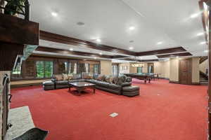 Spacious recreation room featuring red patterned carpeting, recessed lighting, wood-trimmed coffered ceiling, and multiple large windows with exterior views