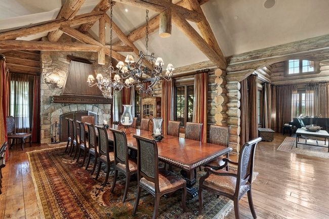 Expansive dining area featuring a stone fireplace with a wood mantel, exposed log beam ceiling, and wood-finish flooring