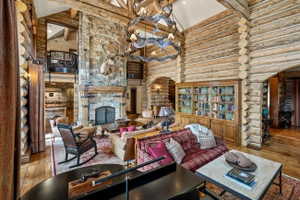 Spacious room featuring log wall construction, a stone-faced fireplace with a hearth, exposed wooden ceiling beams, and polished wood flooring